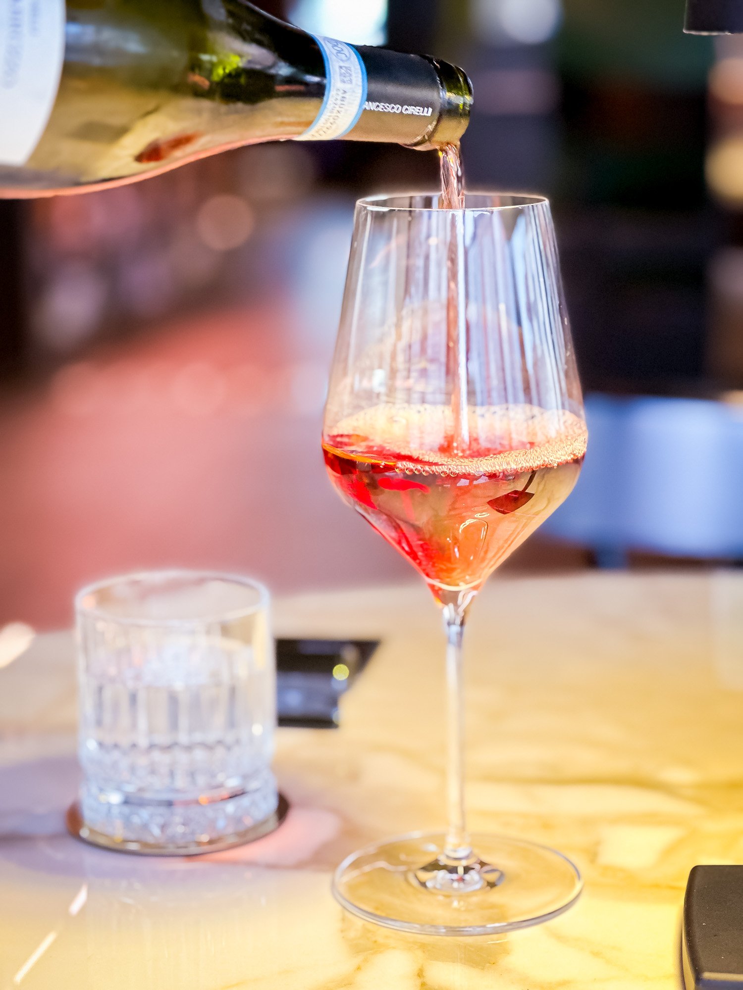 Vino rosato versato in un bicchiere di vino trasparente, con una bottiglia di vino sullo sfondo