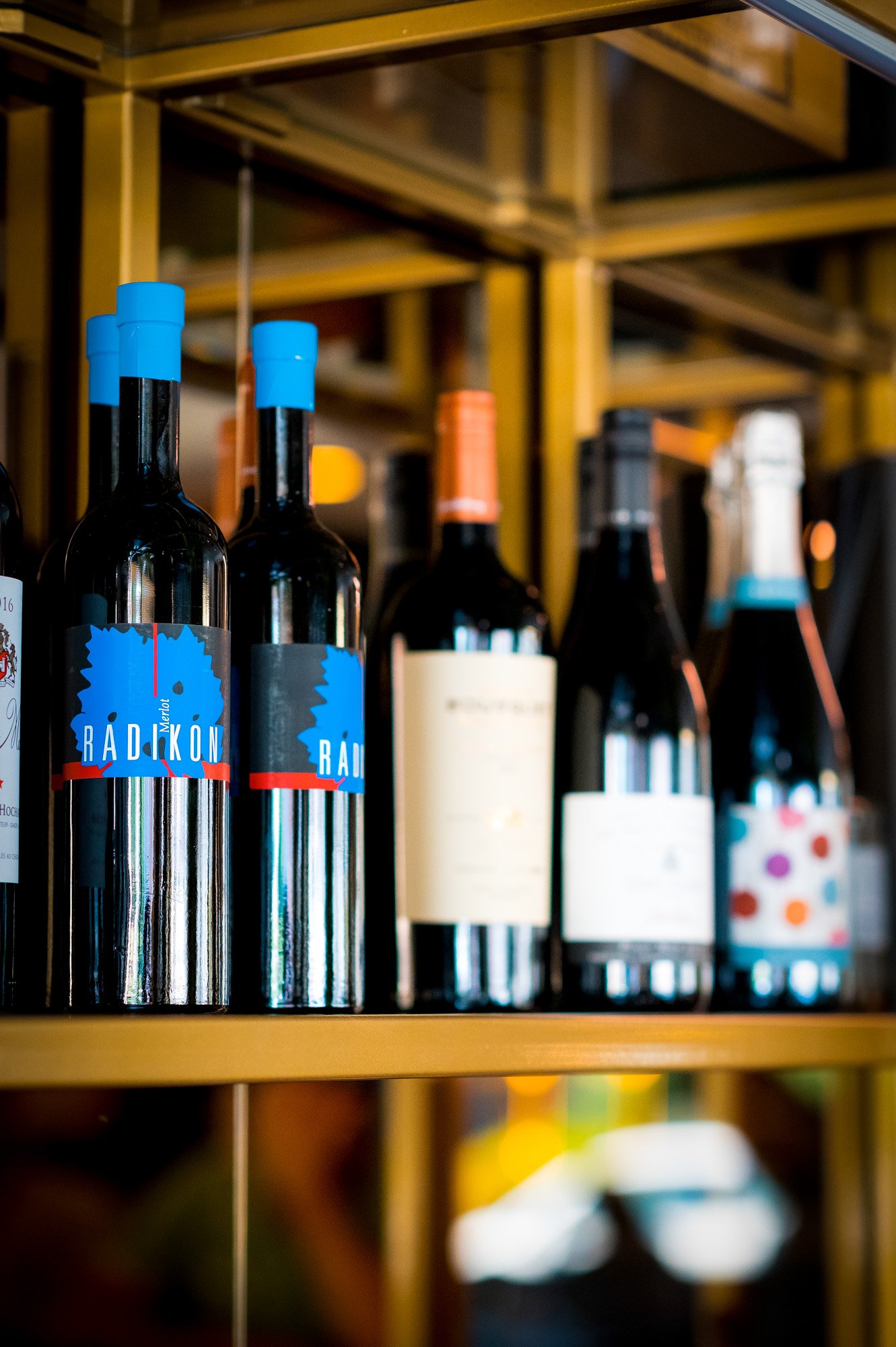 Bottiglie di vino sullo scaffale, alcune con etichette blu e altre con etichette chiare, in un'enoteca