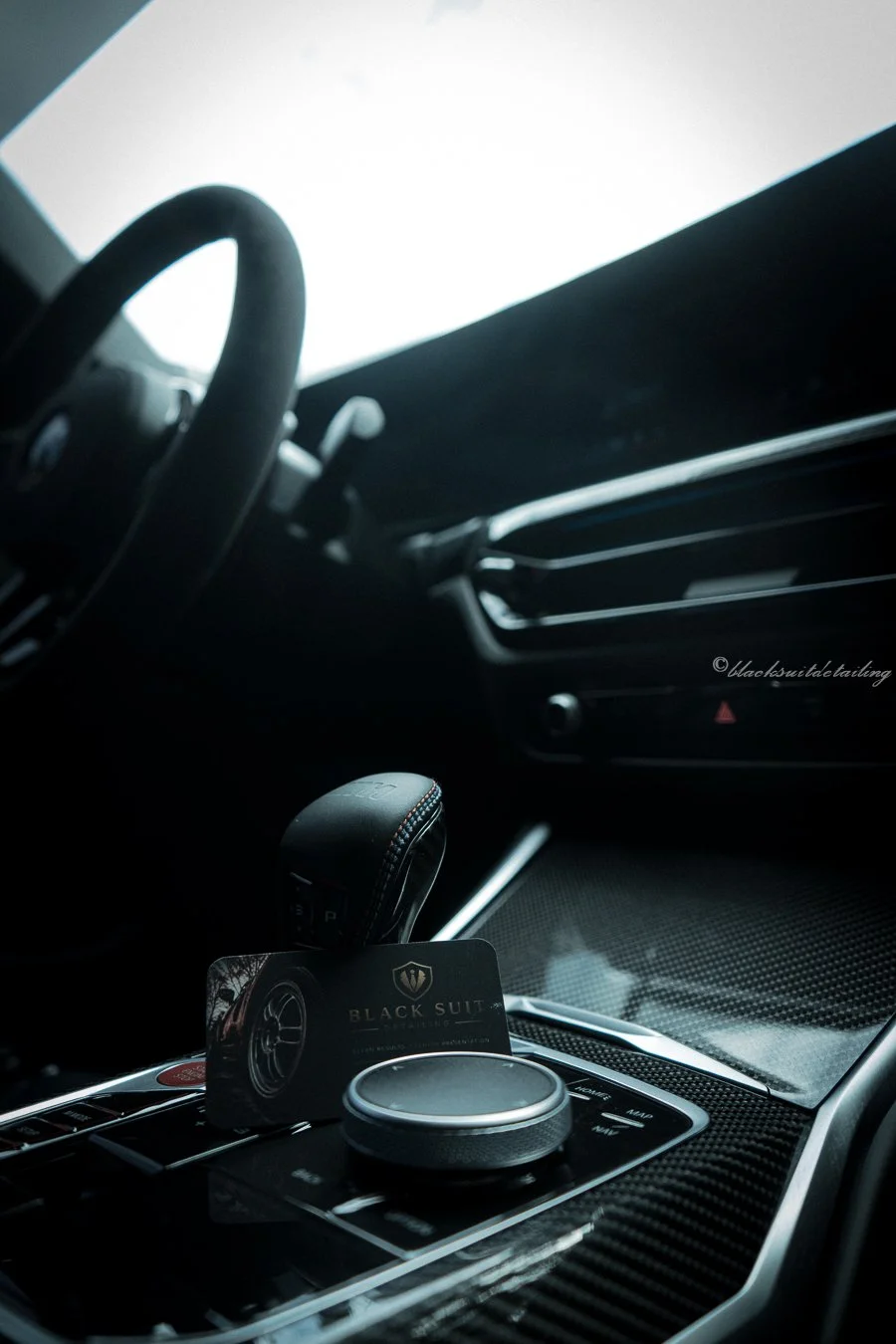 Close-up of the interior of a luxury car, featuring the steering wheel, dashboard, and central console with a Black Suit car accessory.