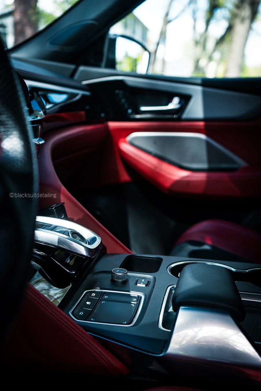 Interior of a luxury car with a red and black dashboard and various control buttons on the center console, partially showing a gear shift and steering wheel.