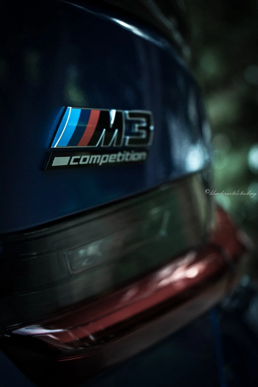 Close-up of a BMW M3 Competition badge on a dark blue car.