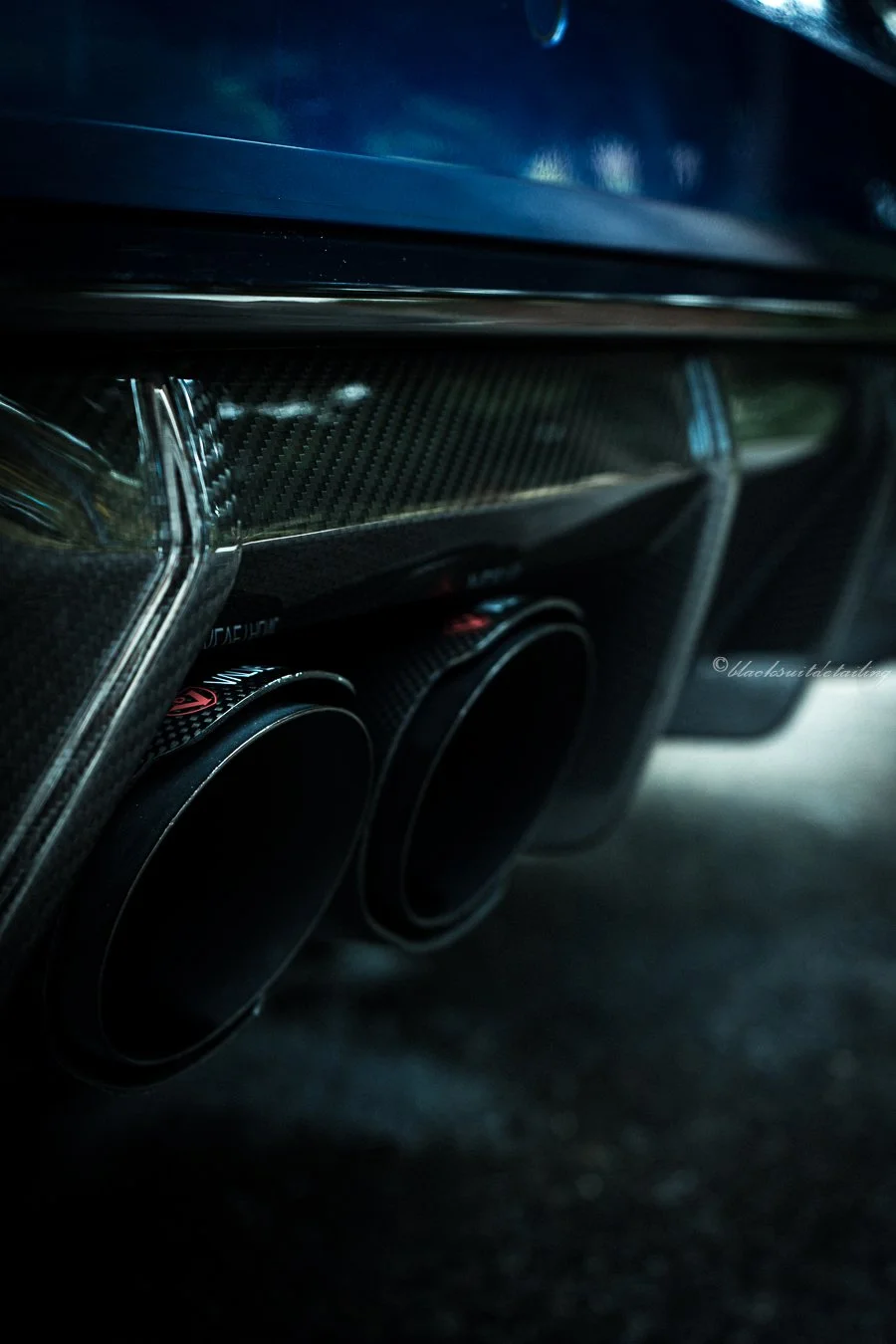 Close-up of a high-performance car's carbon fiber rear diffuser and dual exhaust pipes.