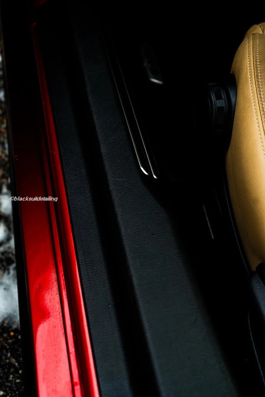 Close-up of car interior showing a beige seat, black dashboard, and red exterior paint along the door edge.