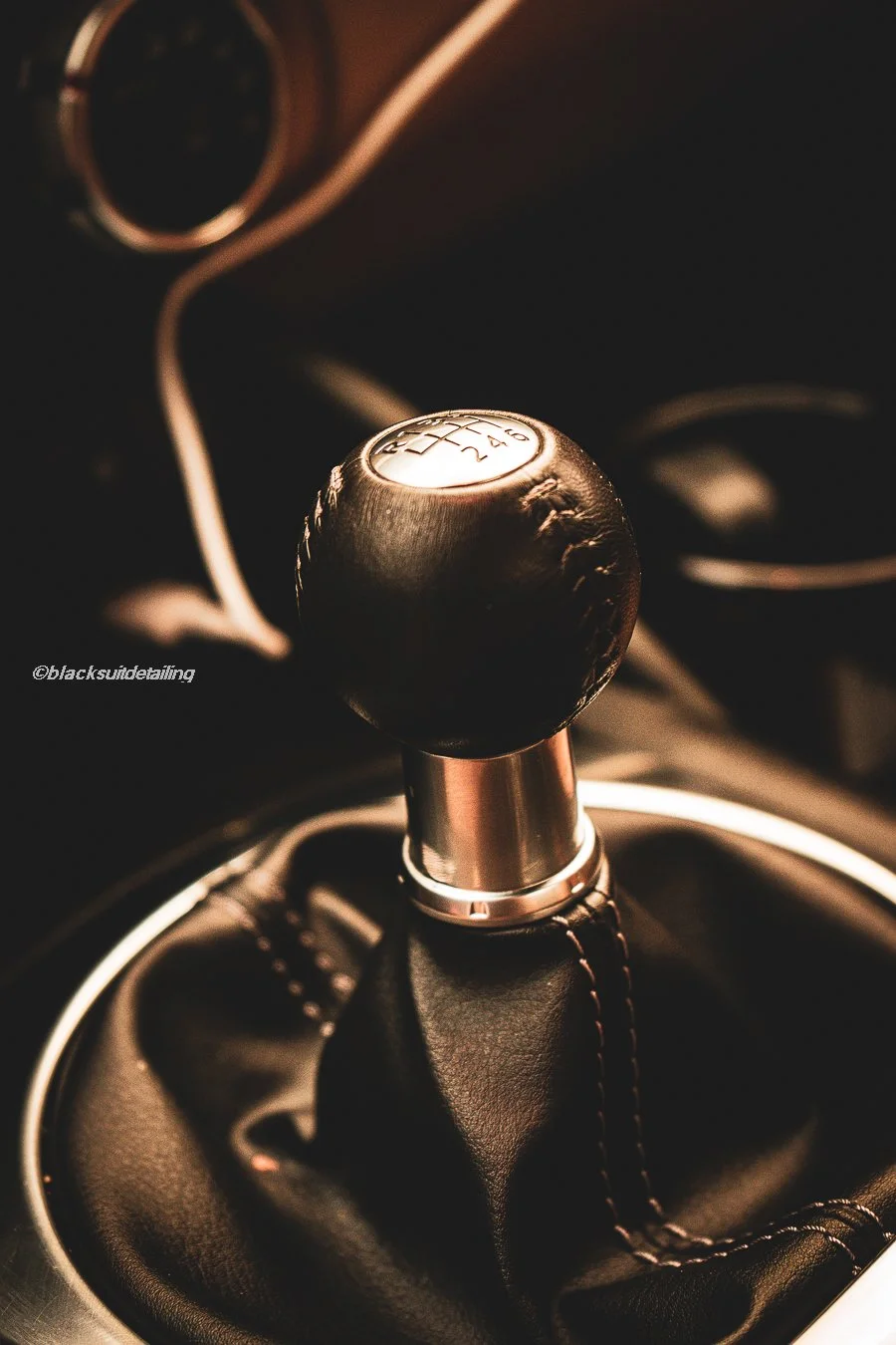 Close-up of a manual gear shifter in a car, showing the gear pattern and leather boot around the gear stick.