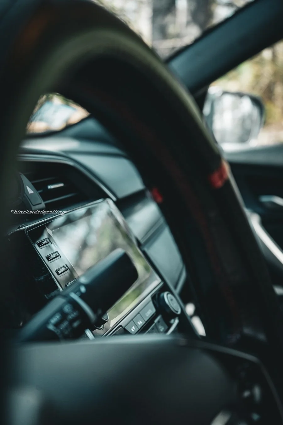 Close-up of a car's interior showing the dashboard, steering wheel, and front window with a blurry view outside.