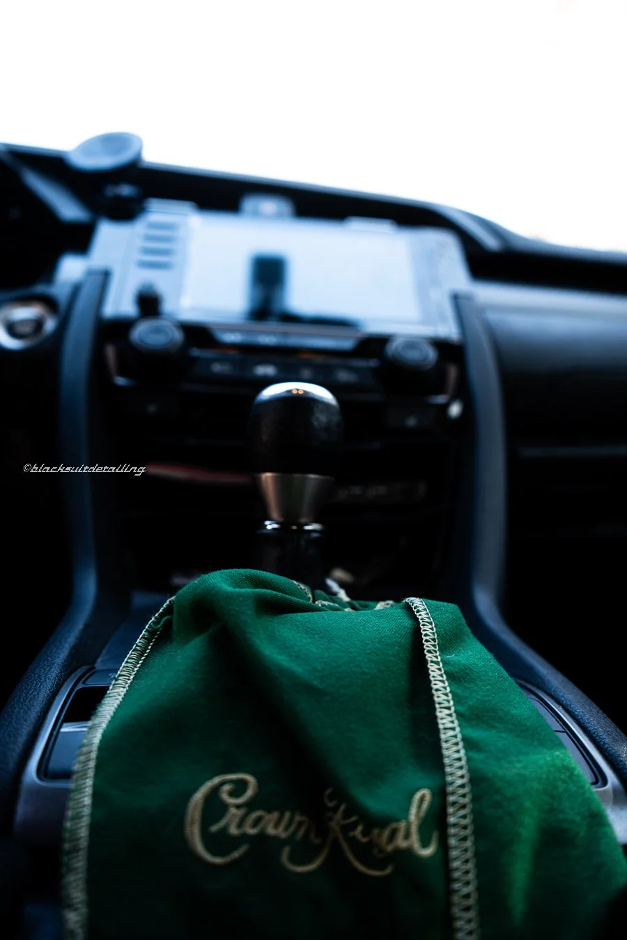 View of the interior of a car from the driver's perspective, showing the gear shift, a green cloth with embroidery, and a blurred dashboard with a smartphone holder.