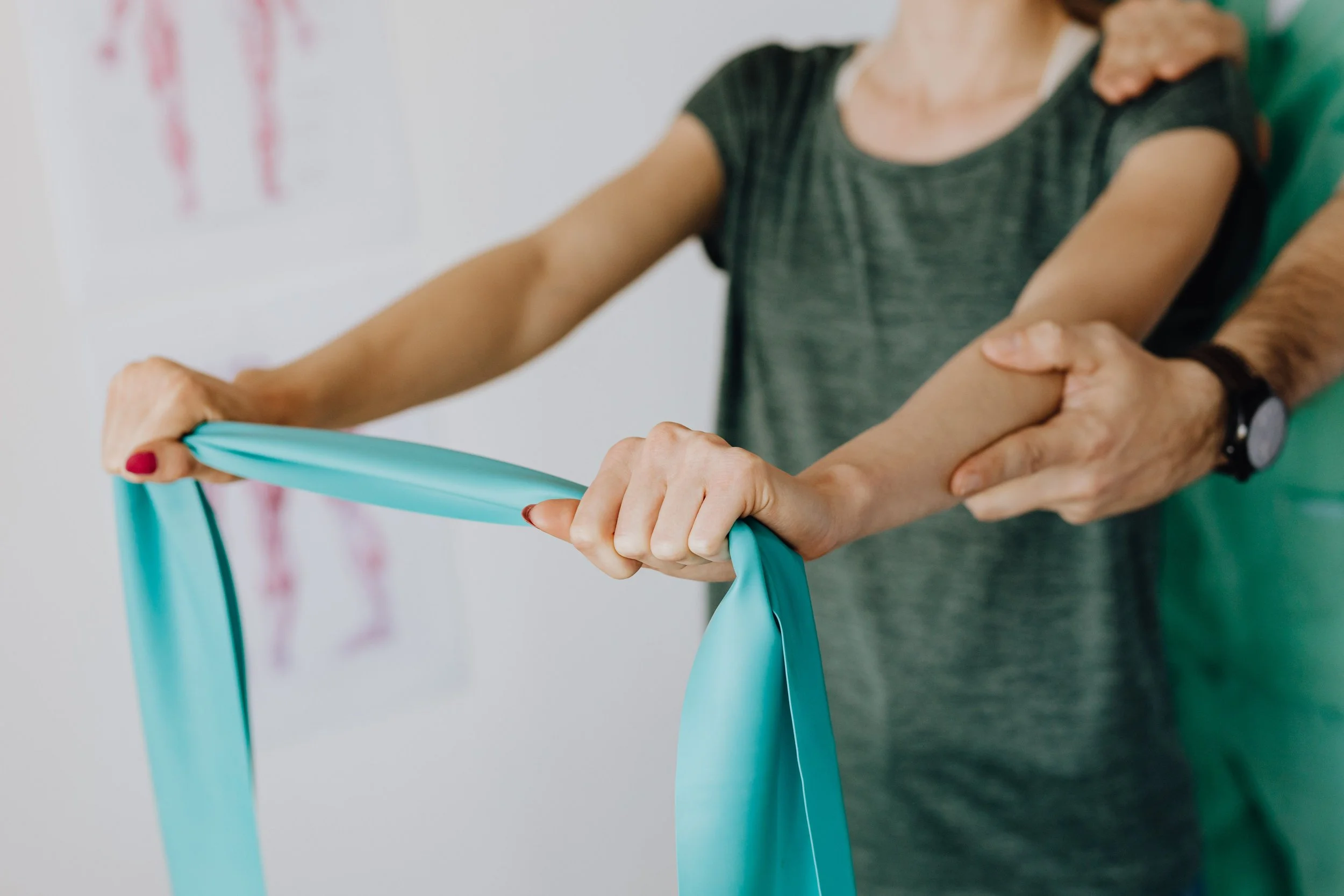 A healthcare worker is assisting an elderly woman with a physical therapy exercise using a blue resistance band.
