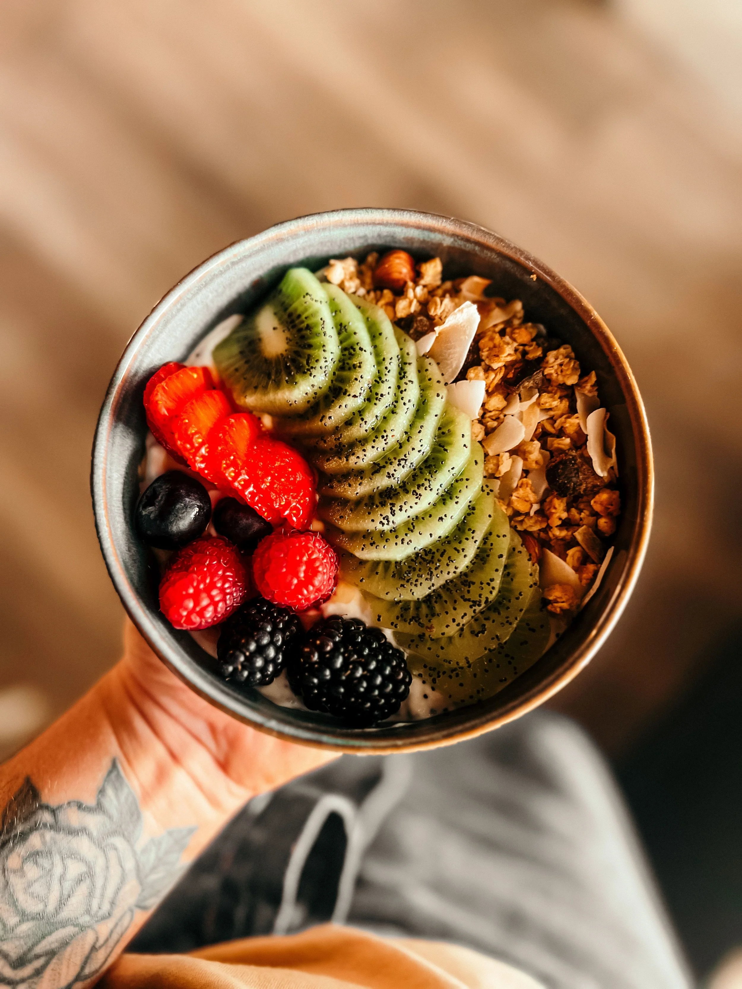 A cup of yogurt topped with sliced kiwi, strawberries, blueberries, granola, and shredded coconut.