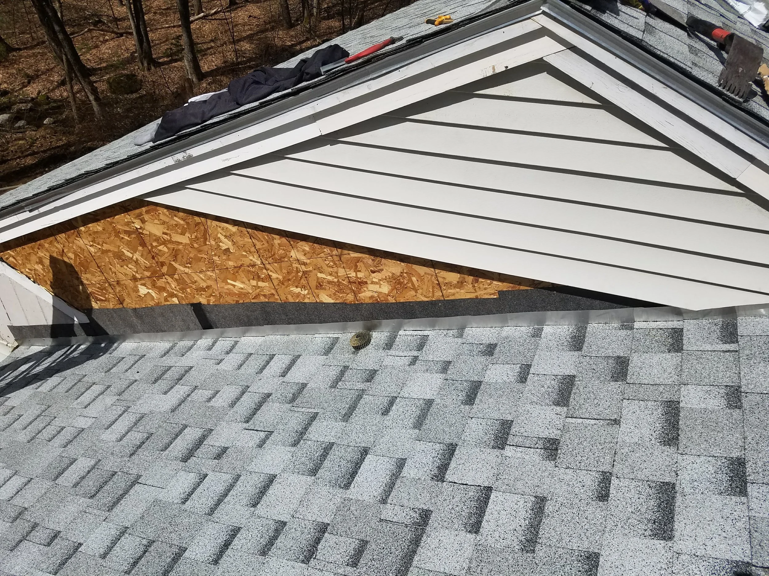Roof with shingles, tools, and materials for roofing repair, including a hammer, screwdriver, and gloves.
