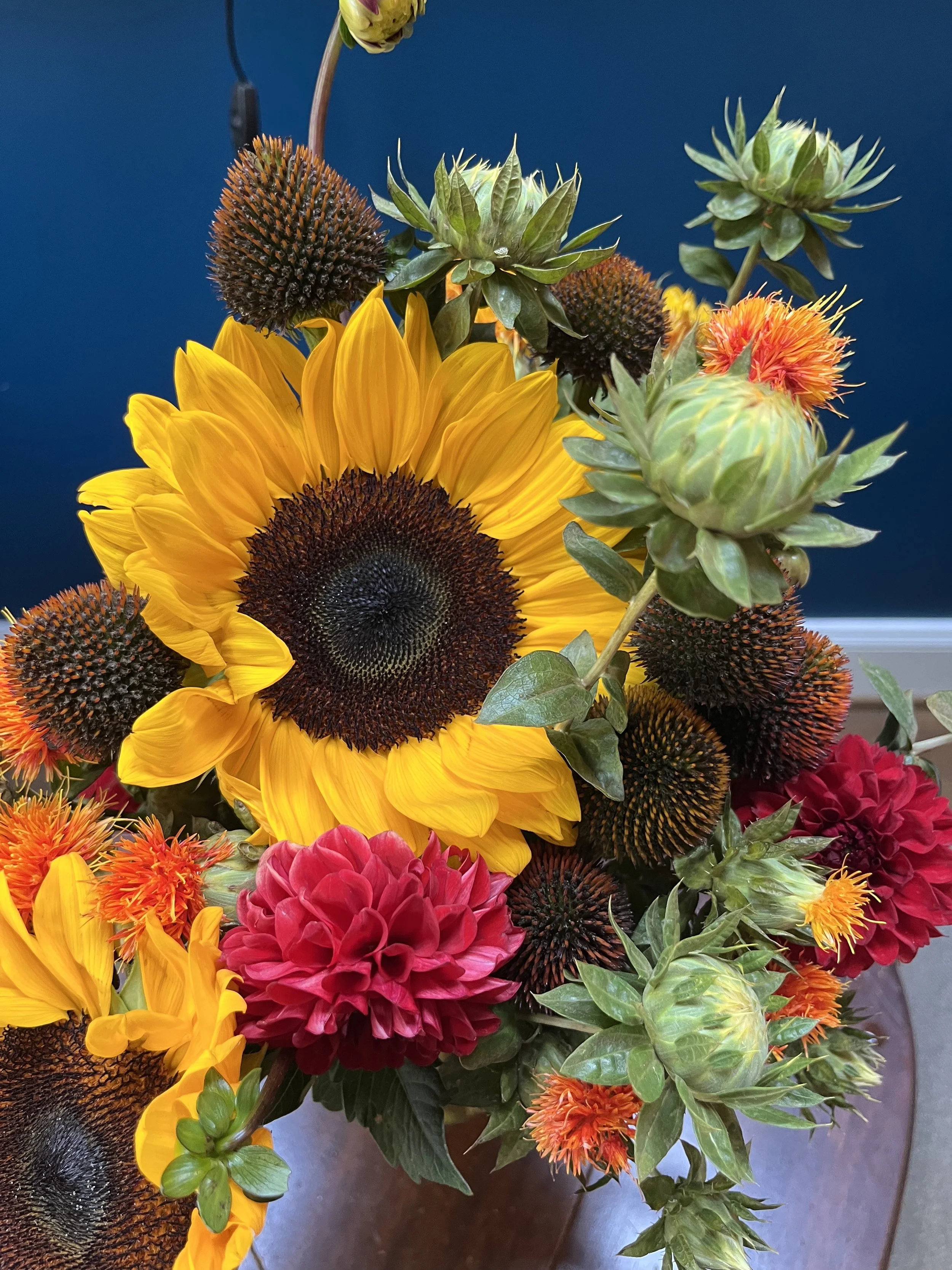 A close up of a bouquet with a sunflower in the center and red and orange flowers around.
