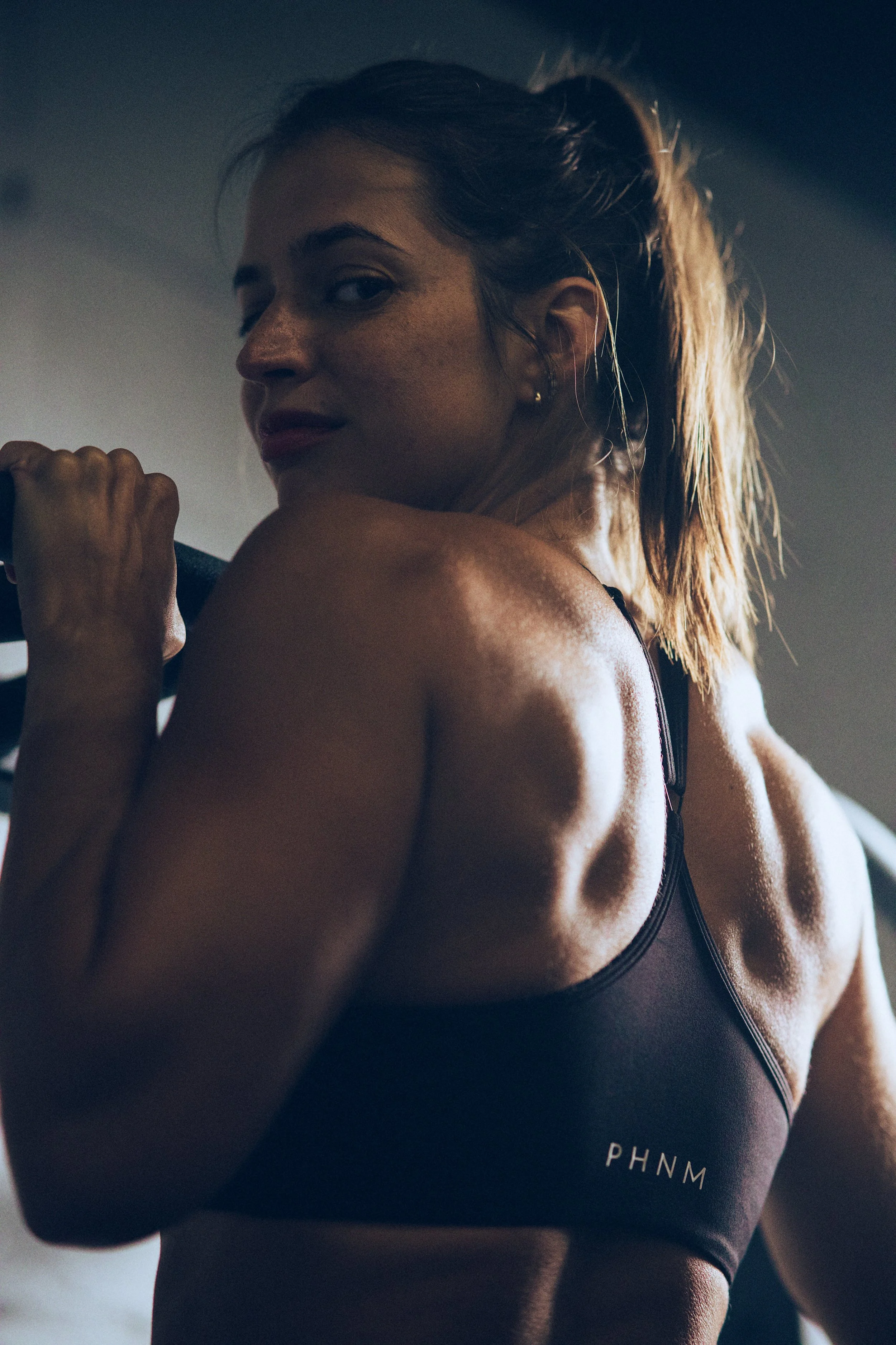 A woman in black sportswear doing pull-ups looking at the camera.