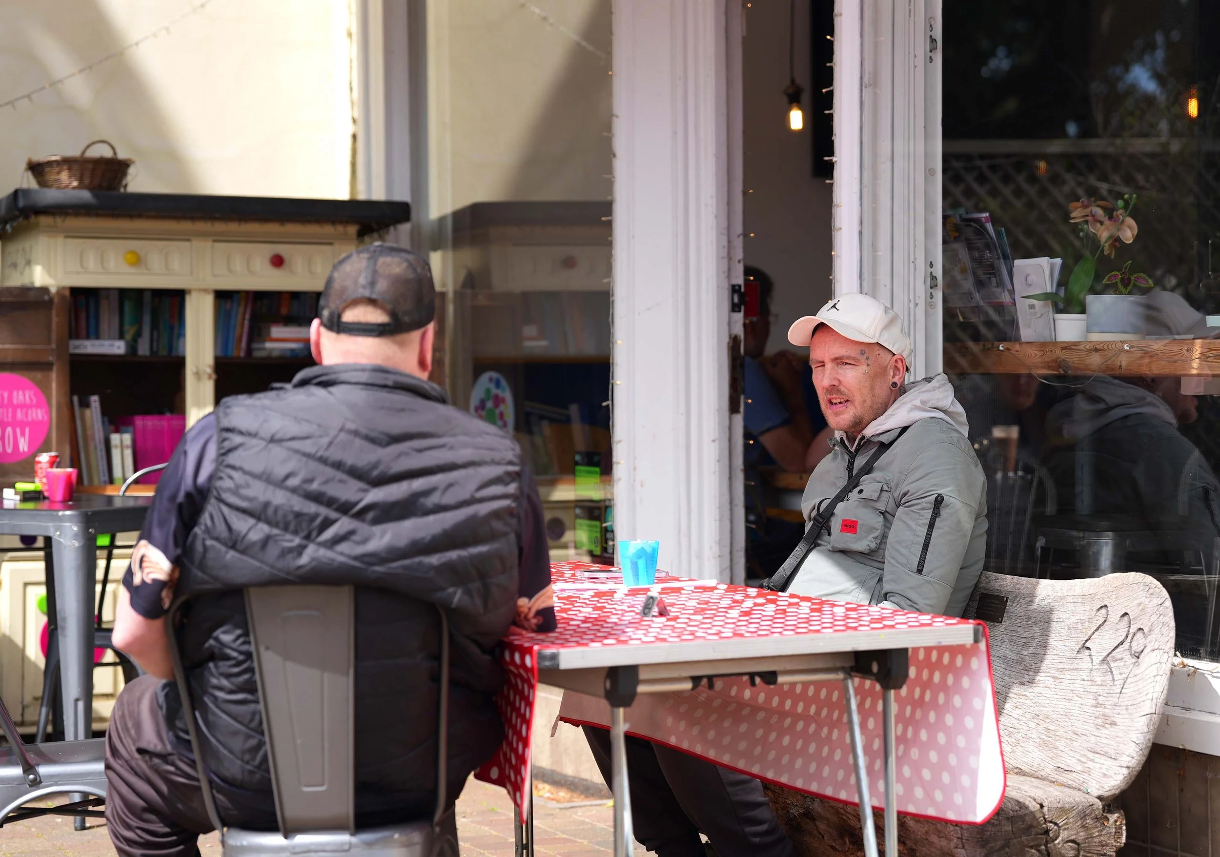 Two men sitting outdoors at a red and white polka dot tablecloth, having a conversation. The Shed group for men, running each Friday in Kempston.