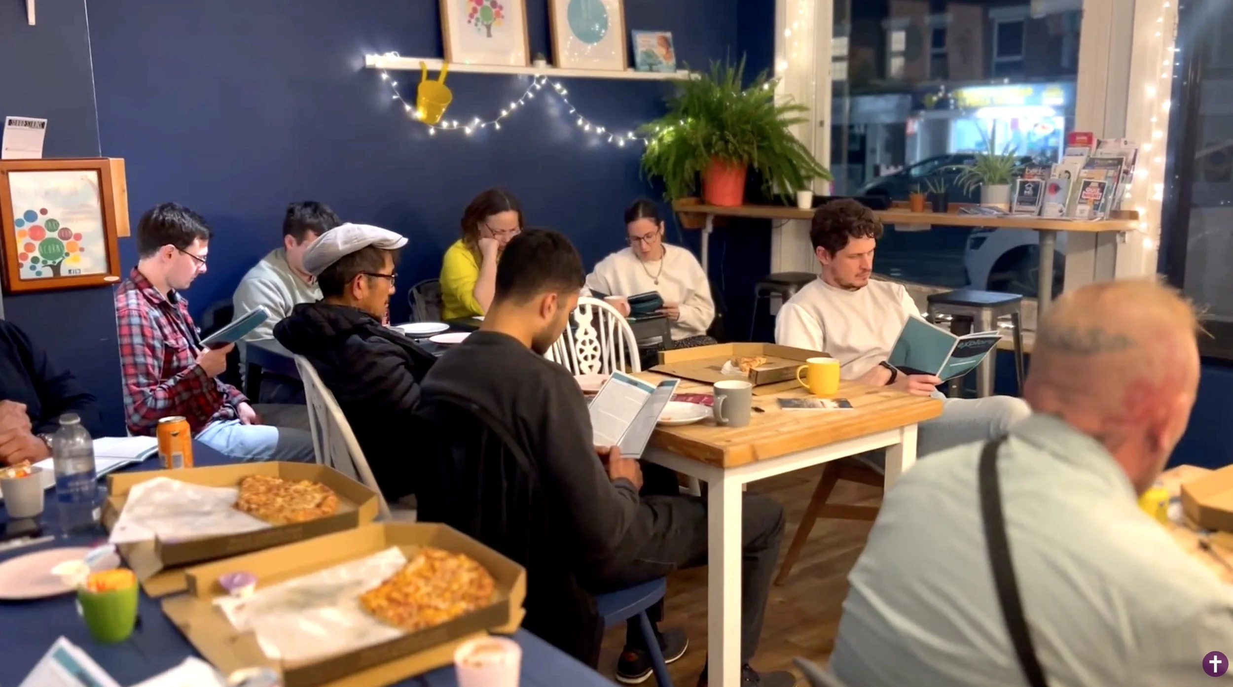 People sitting at tables in a cozy cafe, enjoying pizza and exploring faith and the claims of Christianity. #Explore #Christianity