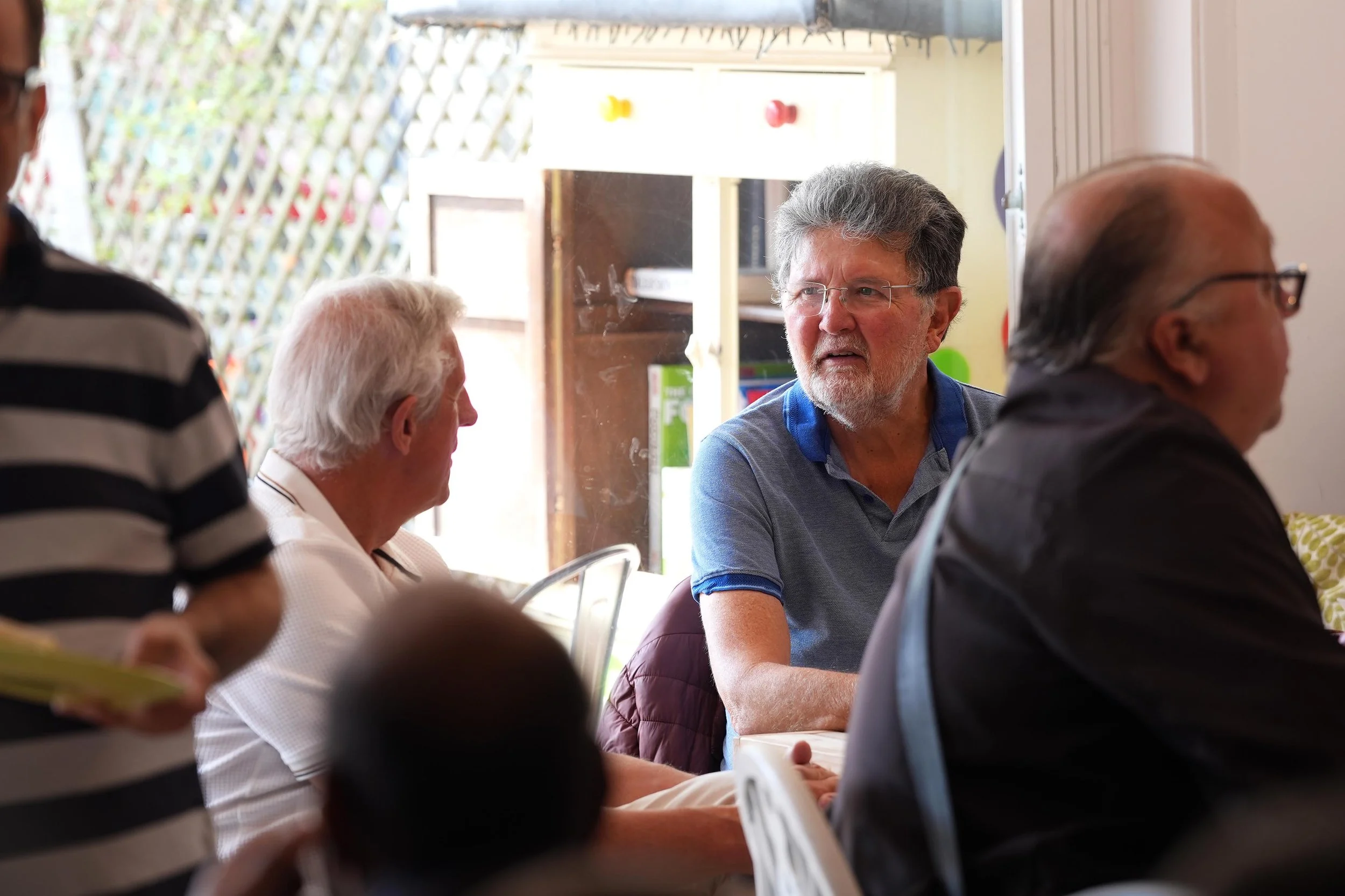 Group of men sitting at a table indoors, engaged in conversation during The Shed, a mens group that runs in Kempston during the week. #Grace #Community #TheShed