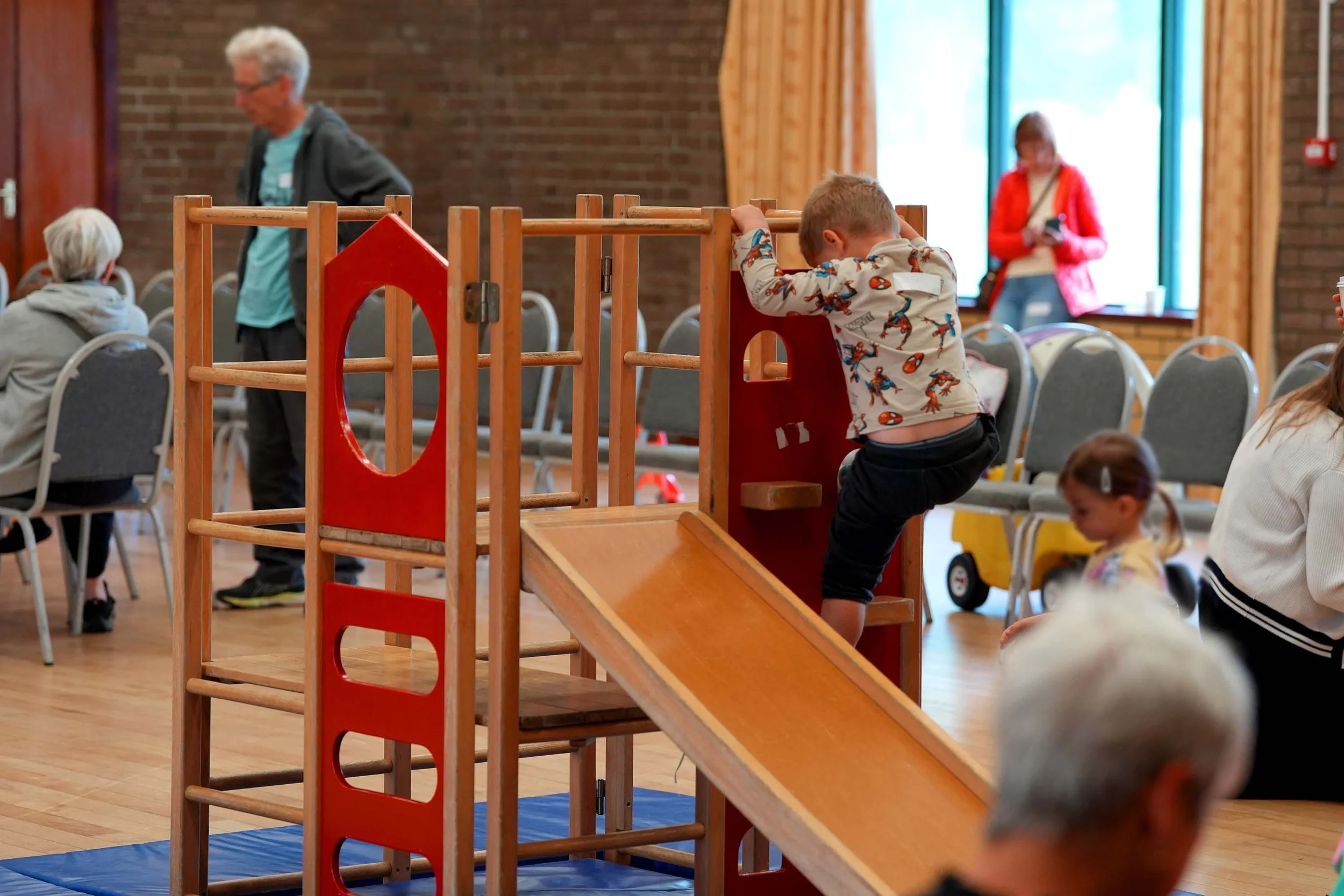 A young boy in a Spider-Man shirt is climbing a small wooden play structure with a slide at 'Playtime' - Grace Community Churches family fun group that runs each week in Kempston. #Family #KidsClubs #Kempston