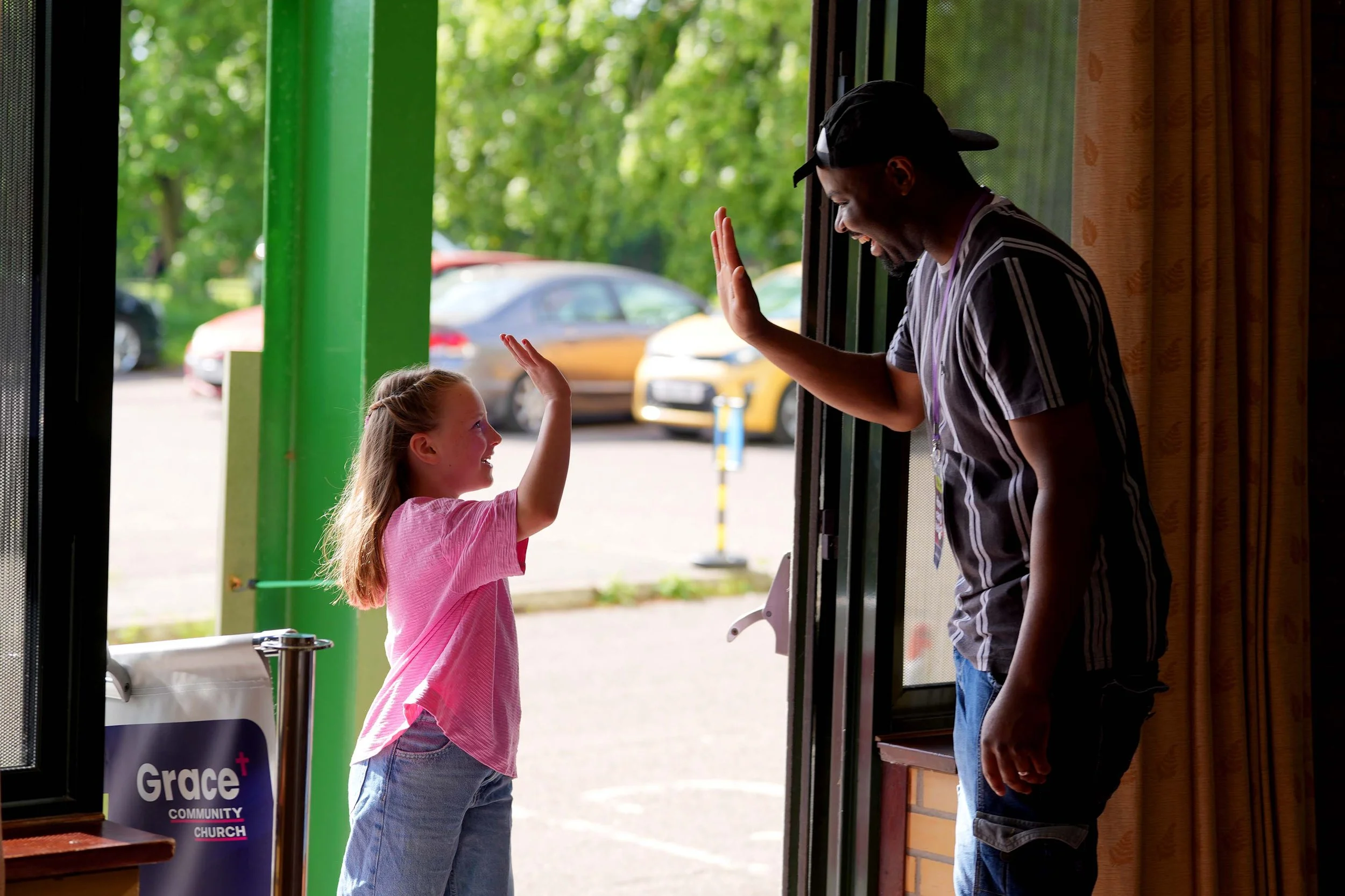 A young girl and a man giving each other a high five at the entrance of Grace Community Church, which meets each week at the Addison Centre in Kempston. #AddisonCentre #Kempston