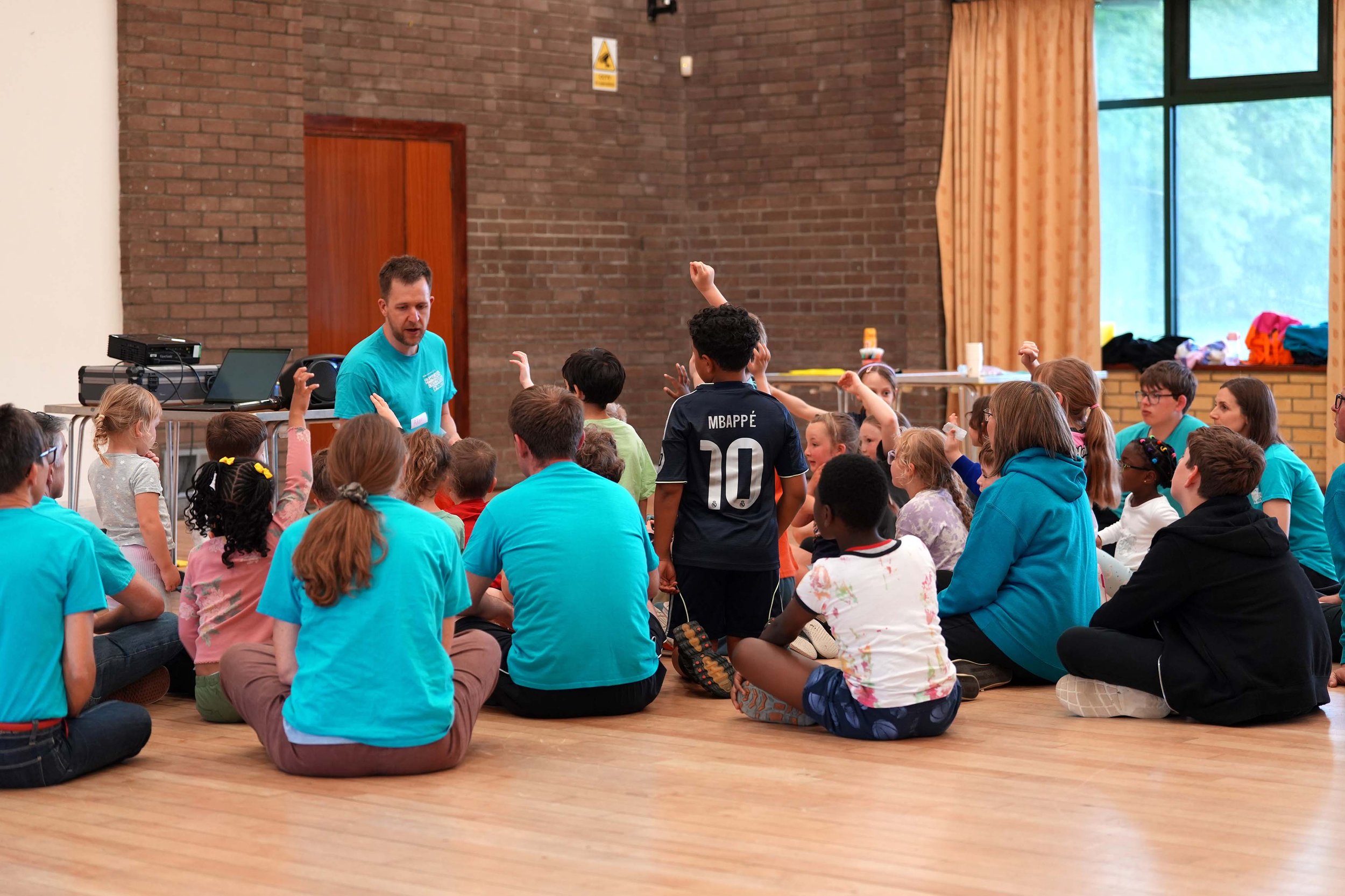 Children and adults sitting on the floor interacting during a Bible story at one of the Children and Youth clubs at Grace.