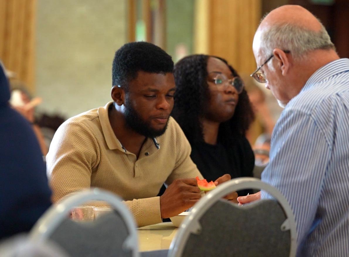 Three people seated at a table engaged in a conversation and eating food together at our 'Big Sunday Lunch'. #community #family