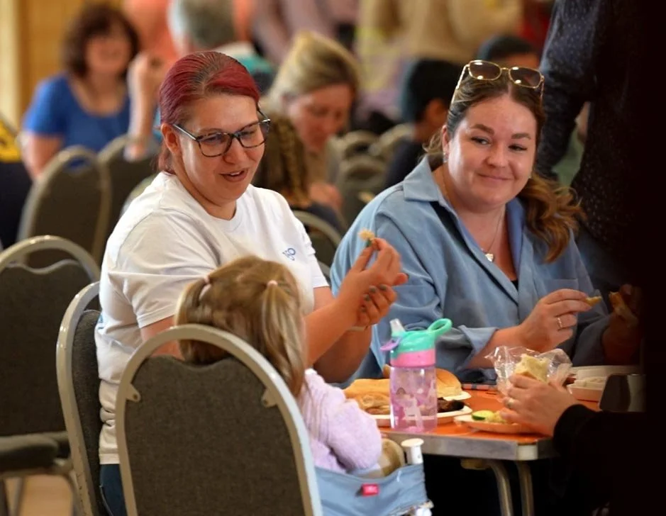Two women seated at a table engaged in a conversation and eating food together at our 'Big Sunday Lunch'. #community #family