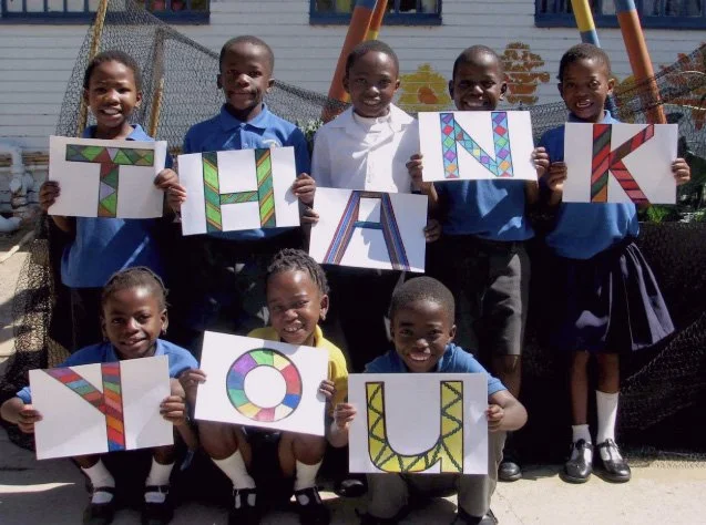 Five children standing outside, holding signs with decorated letters spelling 'THANK YOU'.