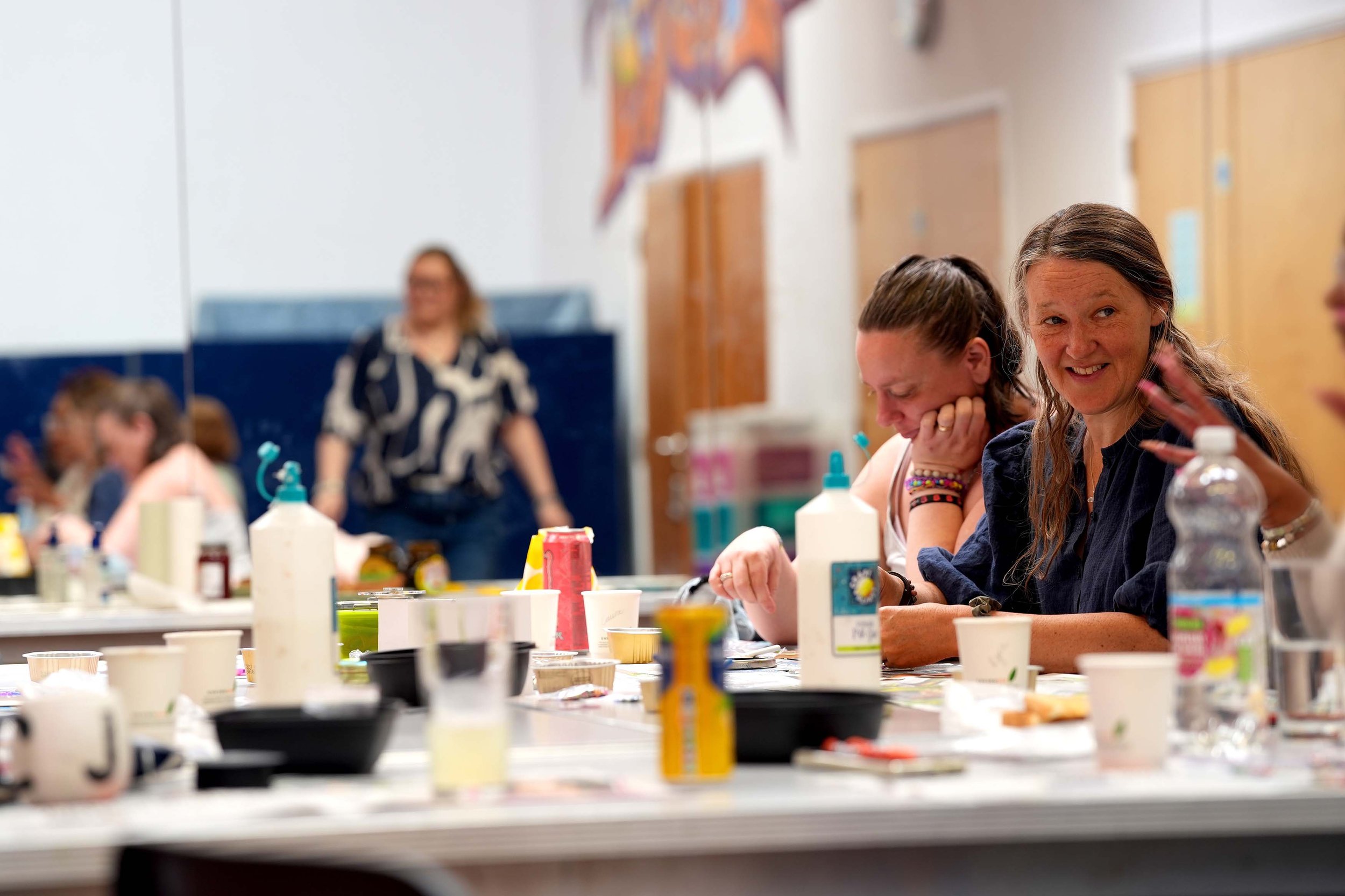Women sitting at a table with various art supplies, smiling and engaging in a creative activity at the Net, Kempston.