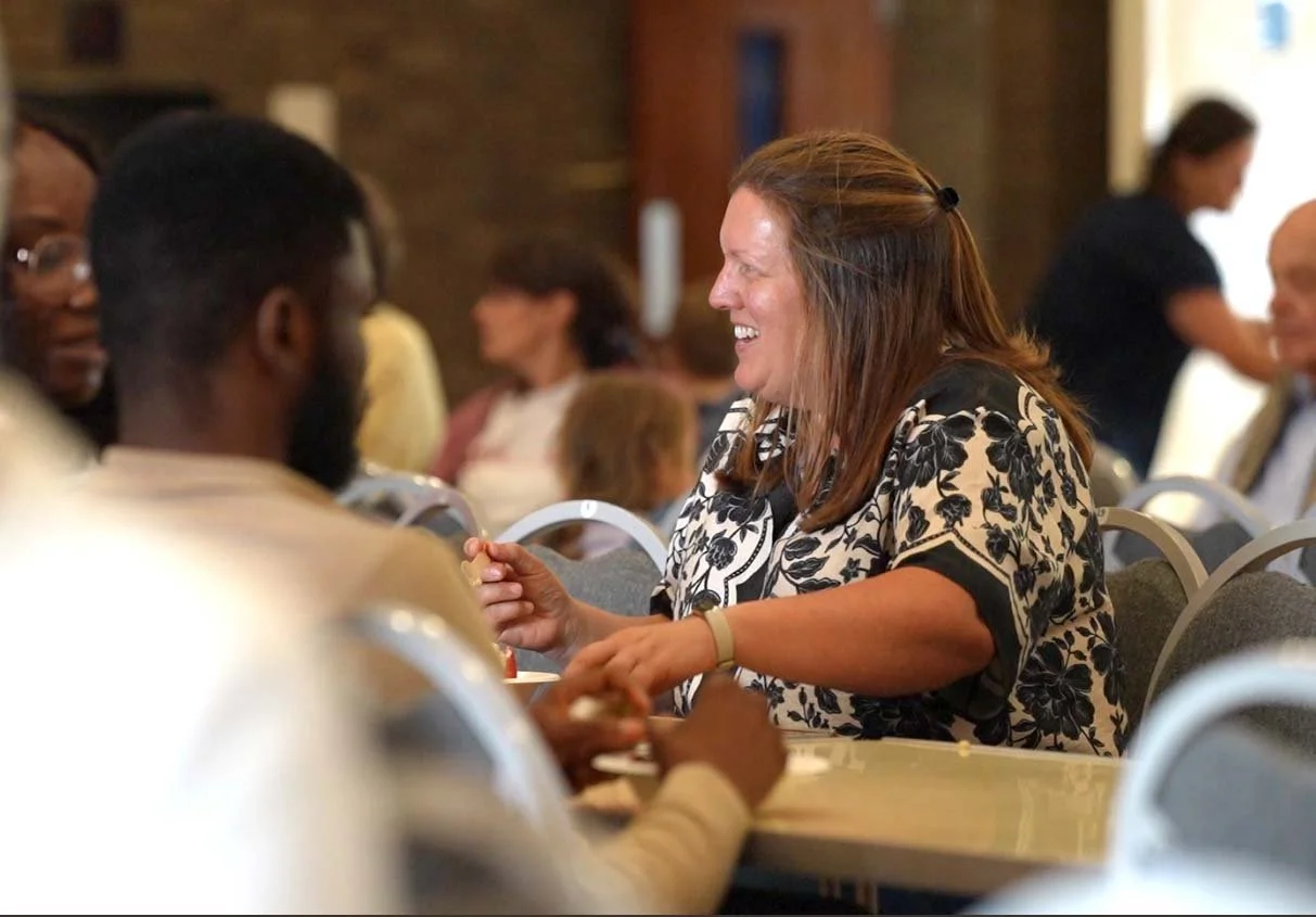A woman with red hair and a floral blouse smiling and talking to a man with dark hair and a beard at the Big Sunday Lunch at Grace