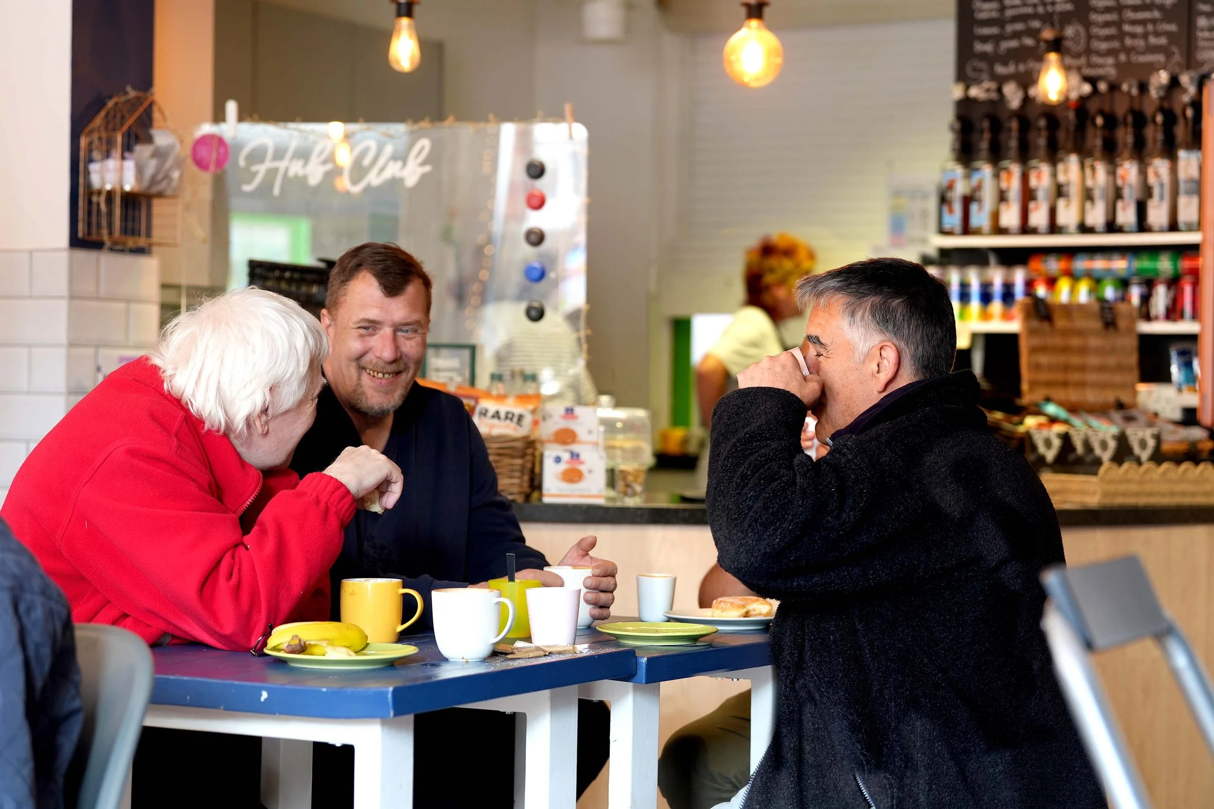 Three people sitting at a table in a café, engaged in conversation - the Shed group for men, running each Friday in Kempston.