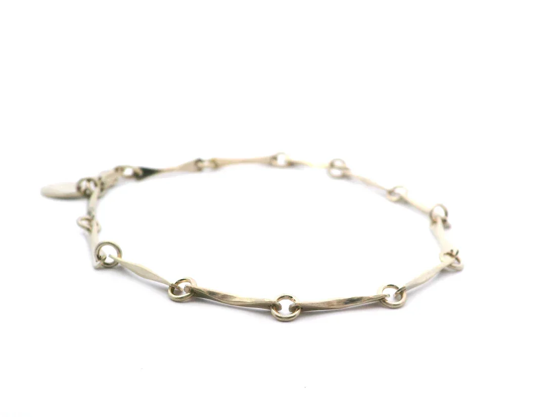 Silver bracelet with multiple elongated, curved links connected by small rings, resting on a white background.