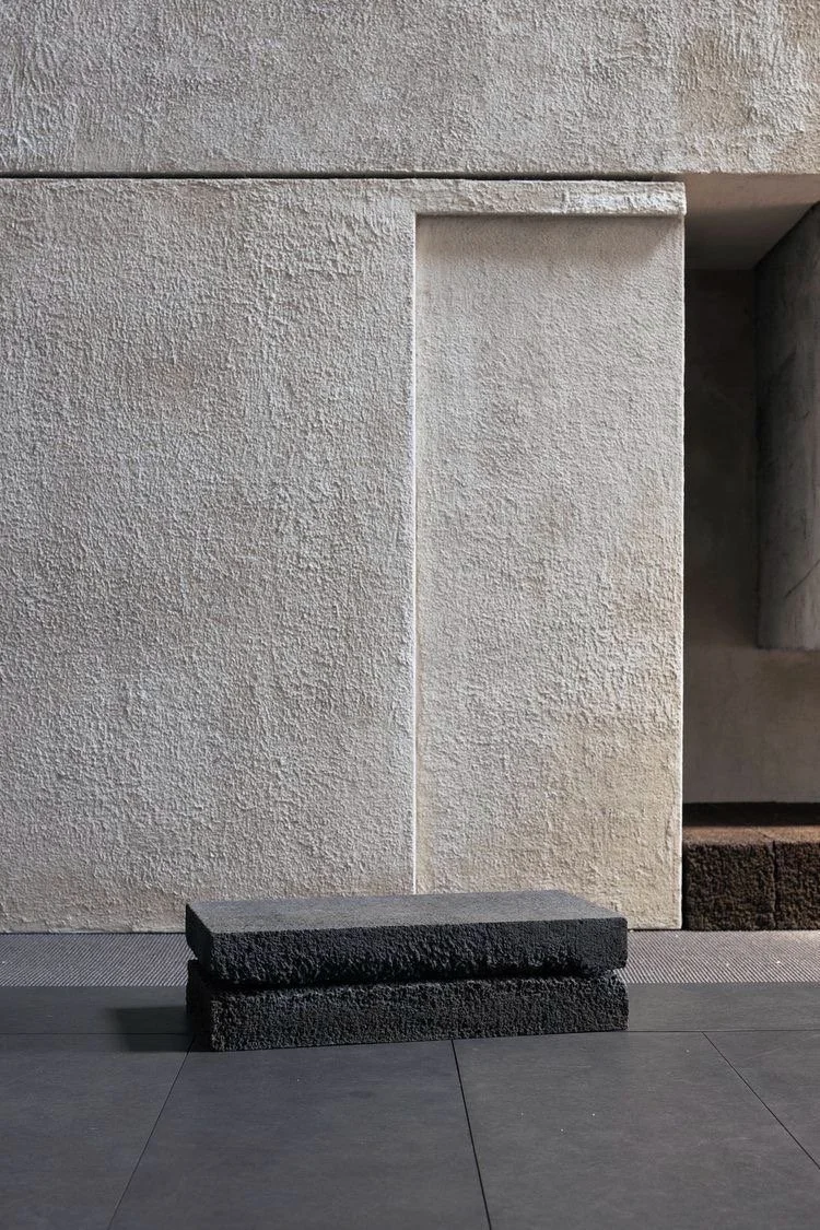 Pareti di pareti di pietra chiara con una fessura centrale e due blocchi di pietra scura sul pavimento.