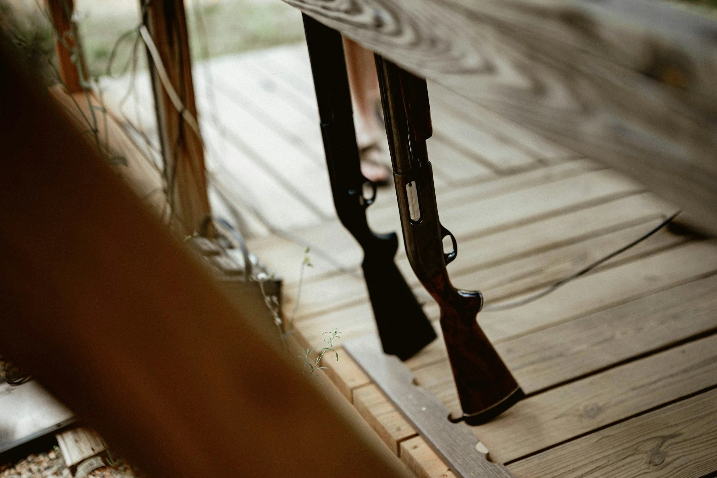 Shot of two black rifles hanging vertically from a surface in an outdoor area with wooden decking.