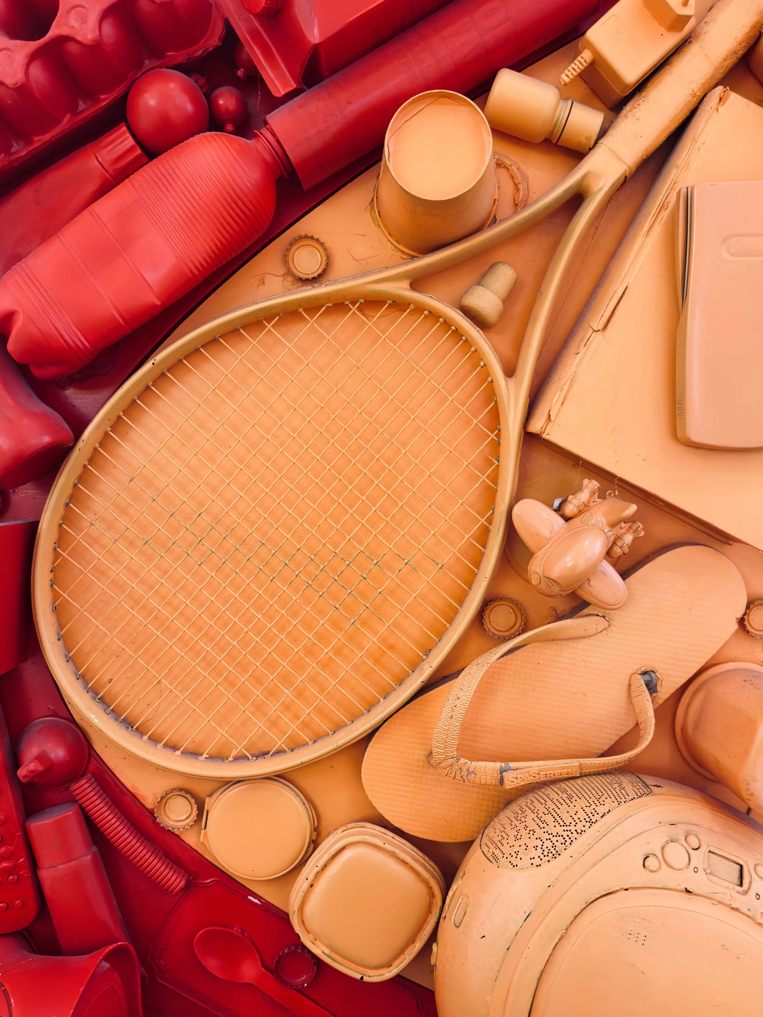 Collection of cream-colored and red plastic household appliances and objects including a tennis racket, a cap, bottles, and various small containers on a surface.