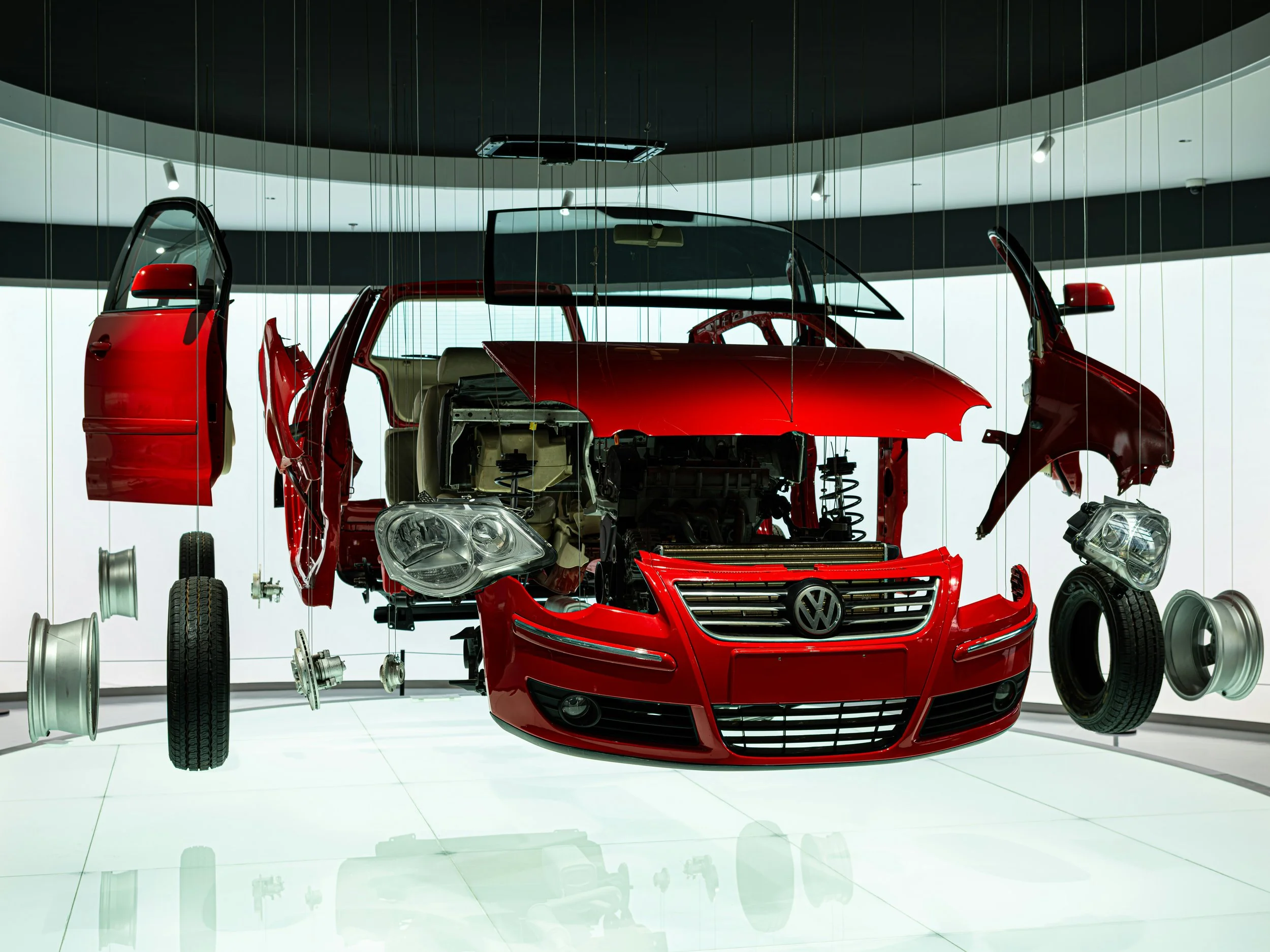 Disassembled red Volkswagen car with parts suspended in a display case.