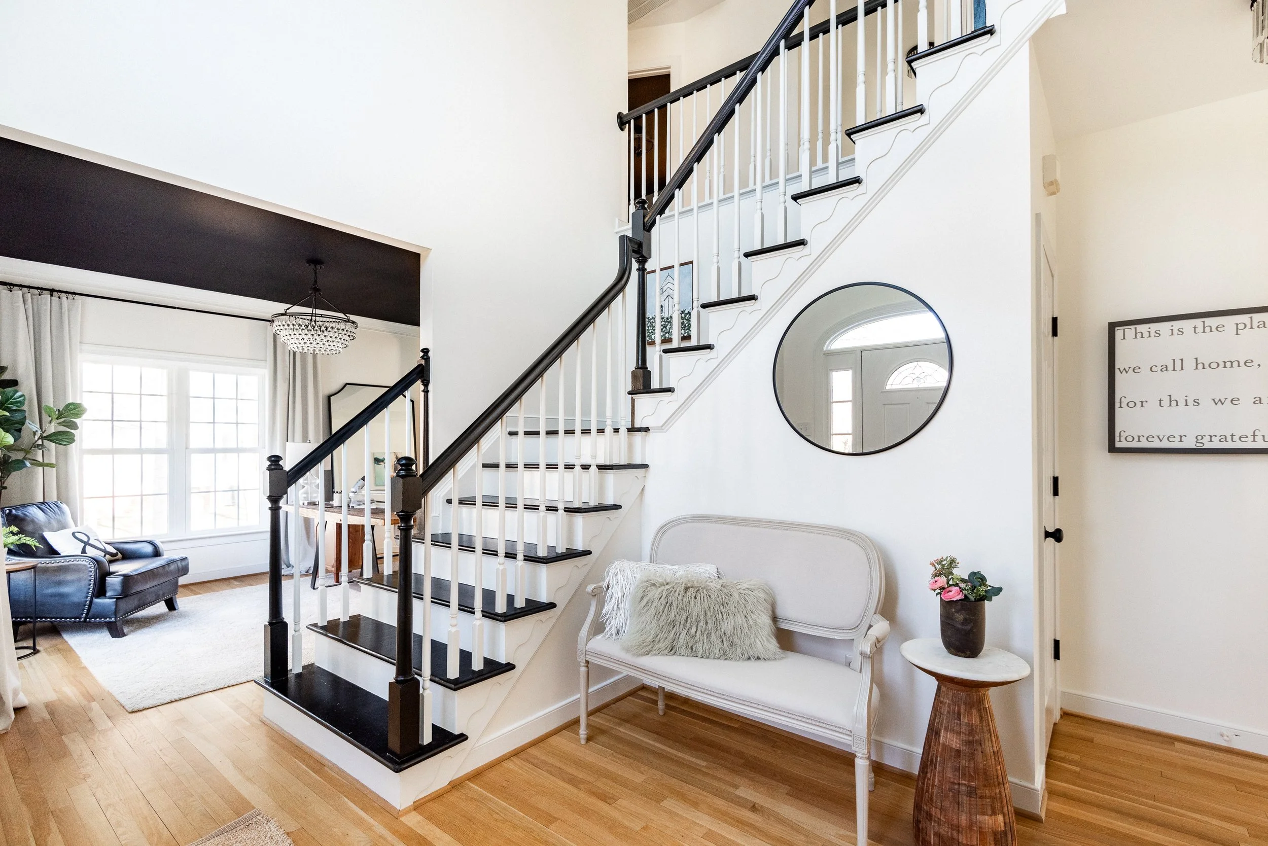Living room with staircase, large window, black and white decor, and floral accents.
