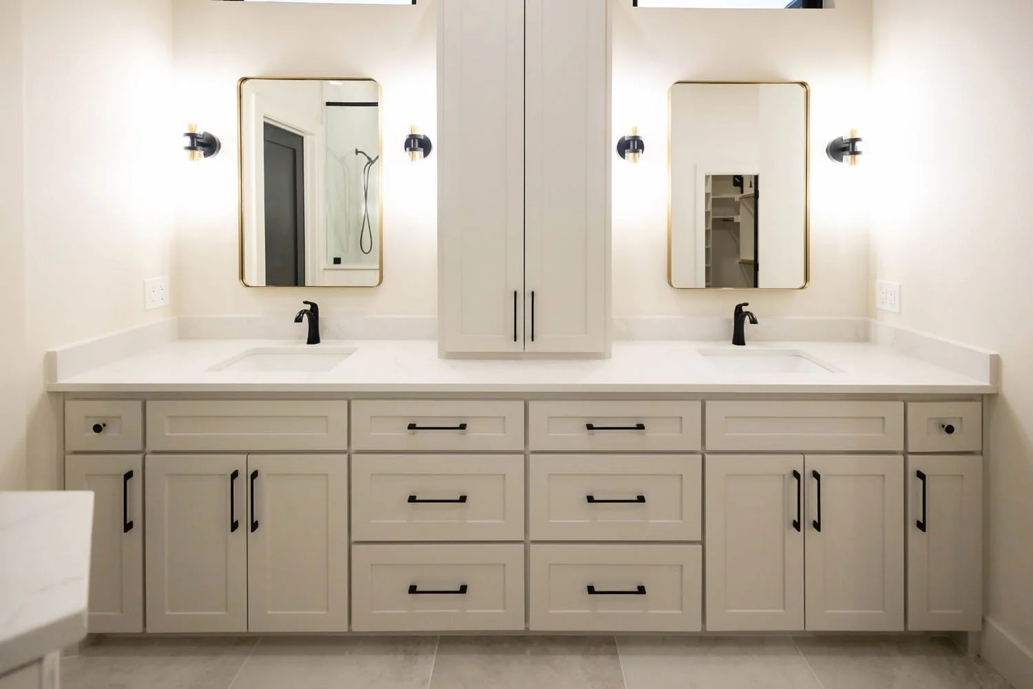 A bright bathroom vanity with dual sinks, white cabinetry, black hardware, and two gold-rimmed rectangular mirrors.