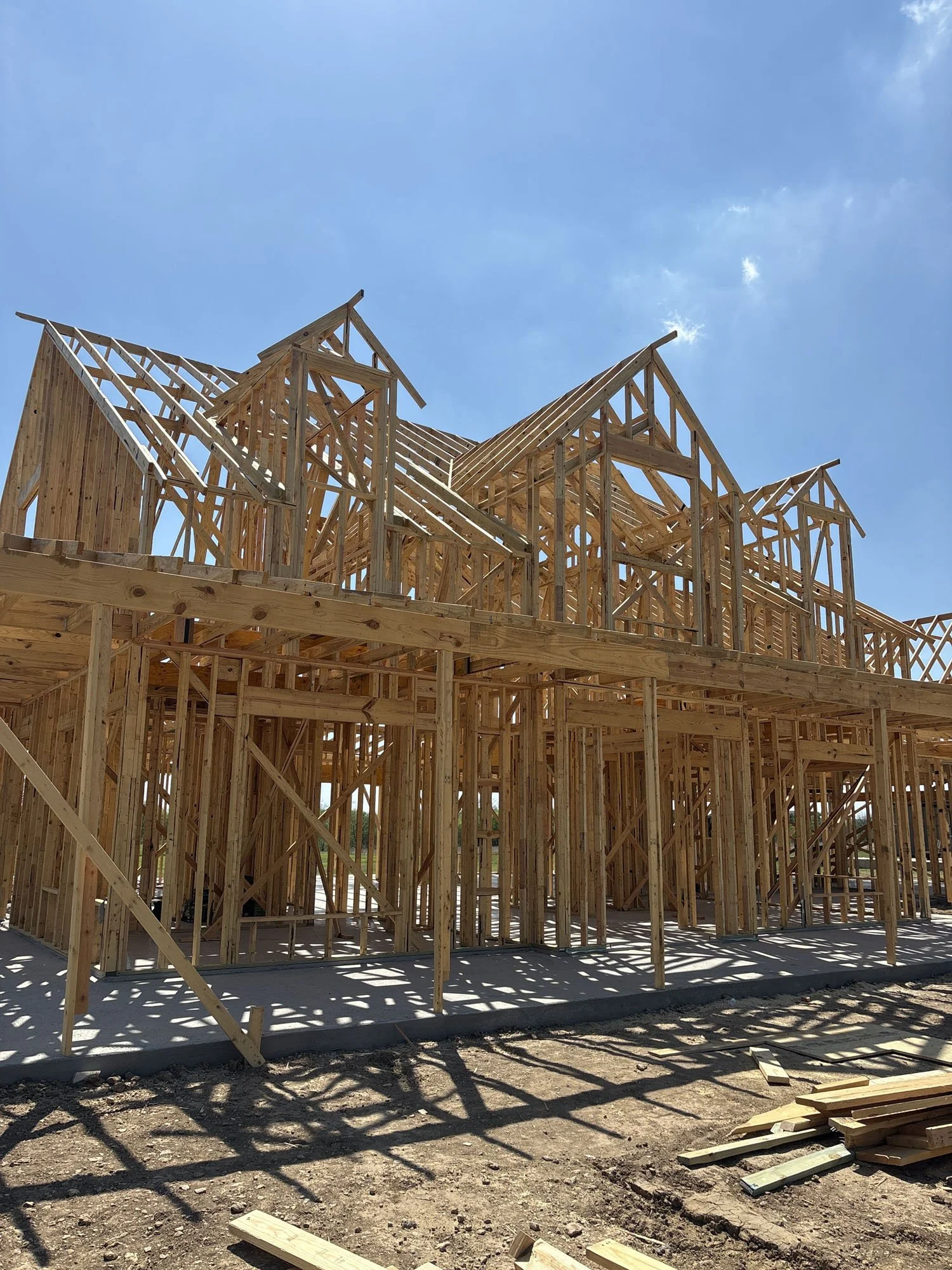 The wooden frame and roof trusses of a new custom home under construction on a sunny day.