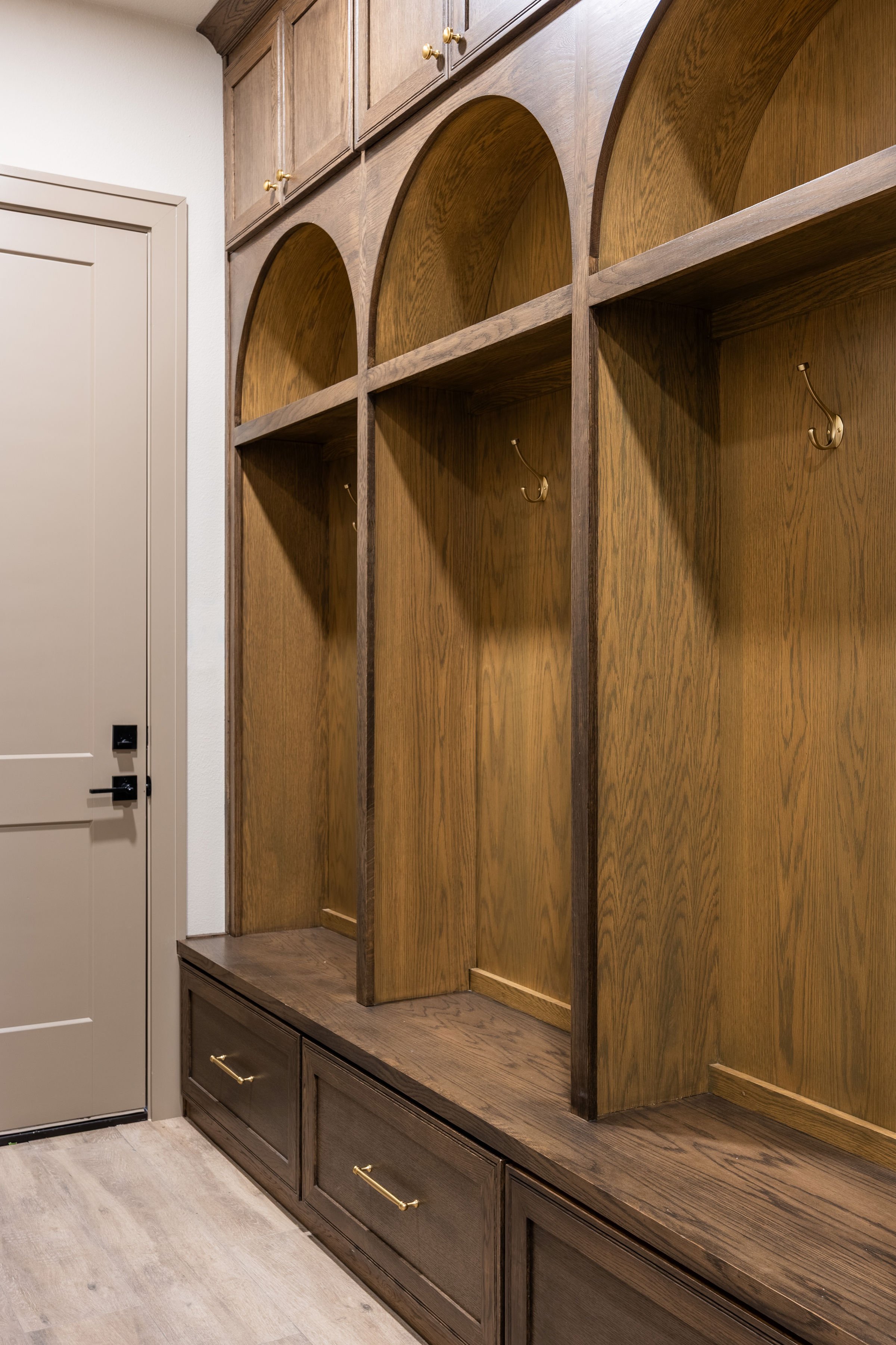 Wooden built-in hall tree with hanging hooks, open shelves, and cabinets at the top, positioned next to a white door with a black handle.
