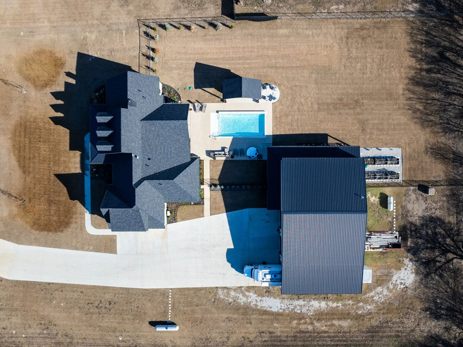 A top-down aerial view of a residential property showing the layout of the home, swimming pool, detached workshop, and concrete driveway.