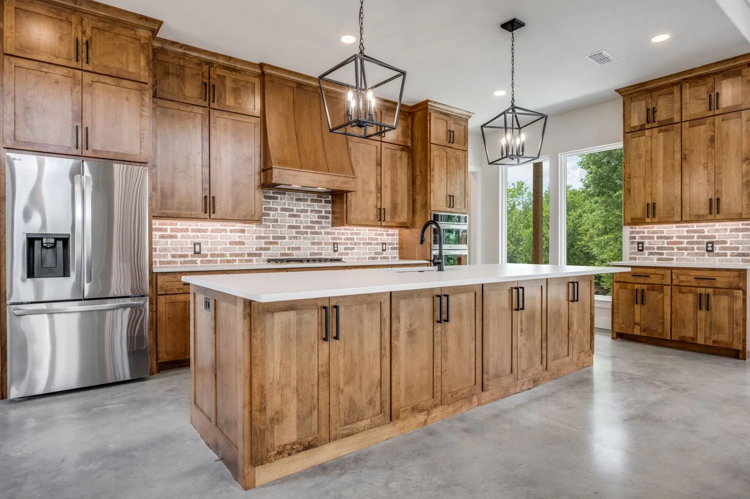 A wide-angle view of a custom kitchen with wood cabinets, stainless steel appliances, and a central island, complemented by polished concrete floors.