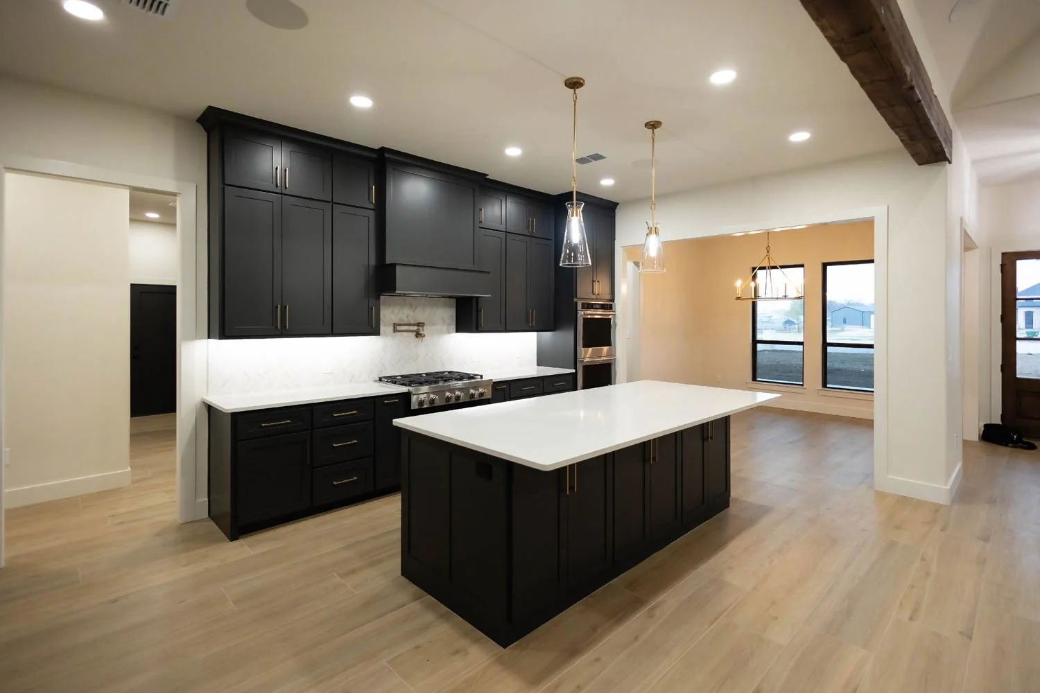 A modern kitchen featuring dark charcoal cabinetry with gold hardware, a white quartz island, and light wood flooring.
