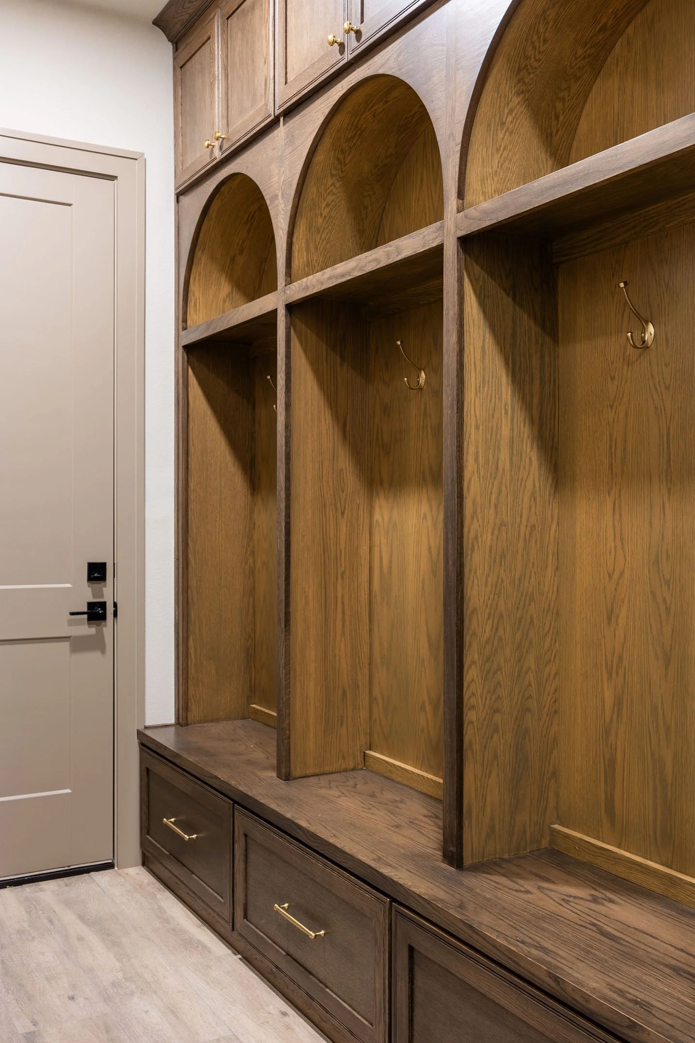A mudroom featuring custom-built wooden lockers with arched openings, brass hooks, and storage drawers.