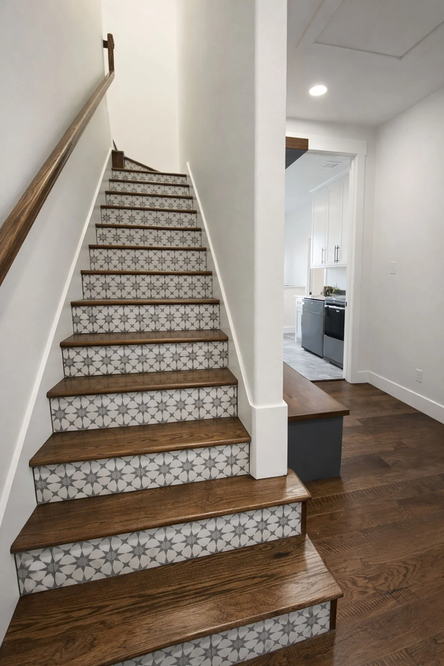 A staircase with dark wood treads and decorative patterned tile risers, leading to an upper level with a view into a laundry area.