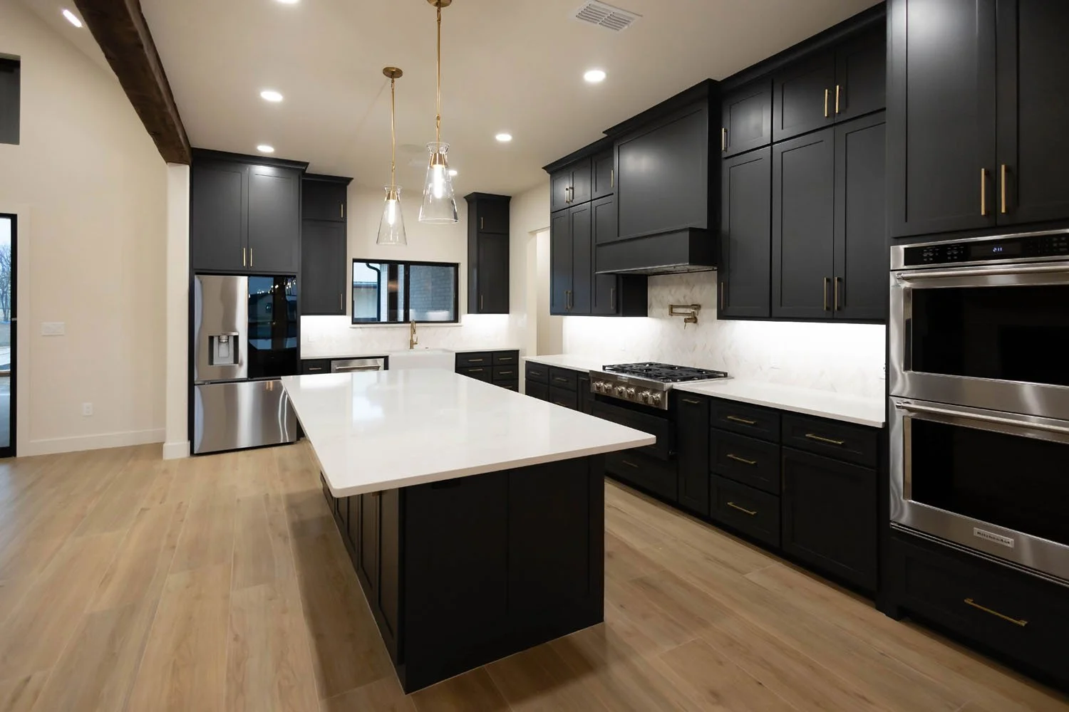 A modern kitchen showcasing floor-to-ceiling black cabinetry, stainless steel appliances, a white farmhouse sink, and a spacious quartz-topped island.