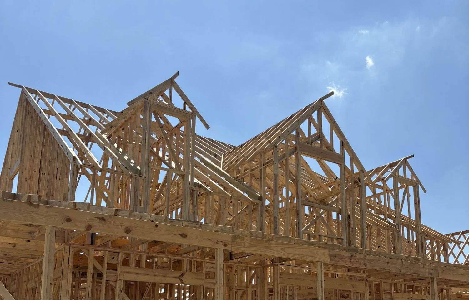 The wooden frame and roof trusses of a new custom home under construction on a sunny day.