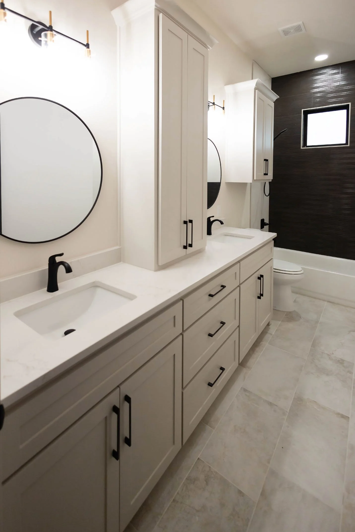 A modern bathroom featuring a white double vanity with black hardware, round mirrors, and a dark tiled shower enclosure.