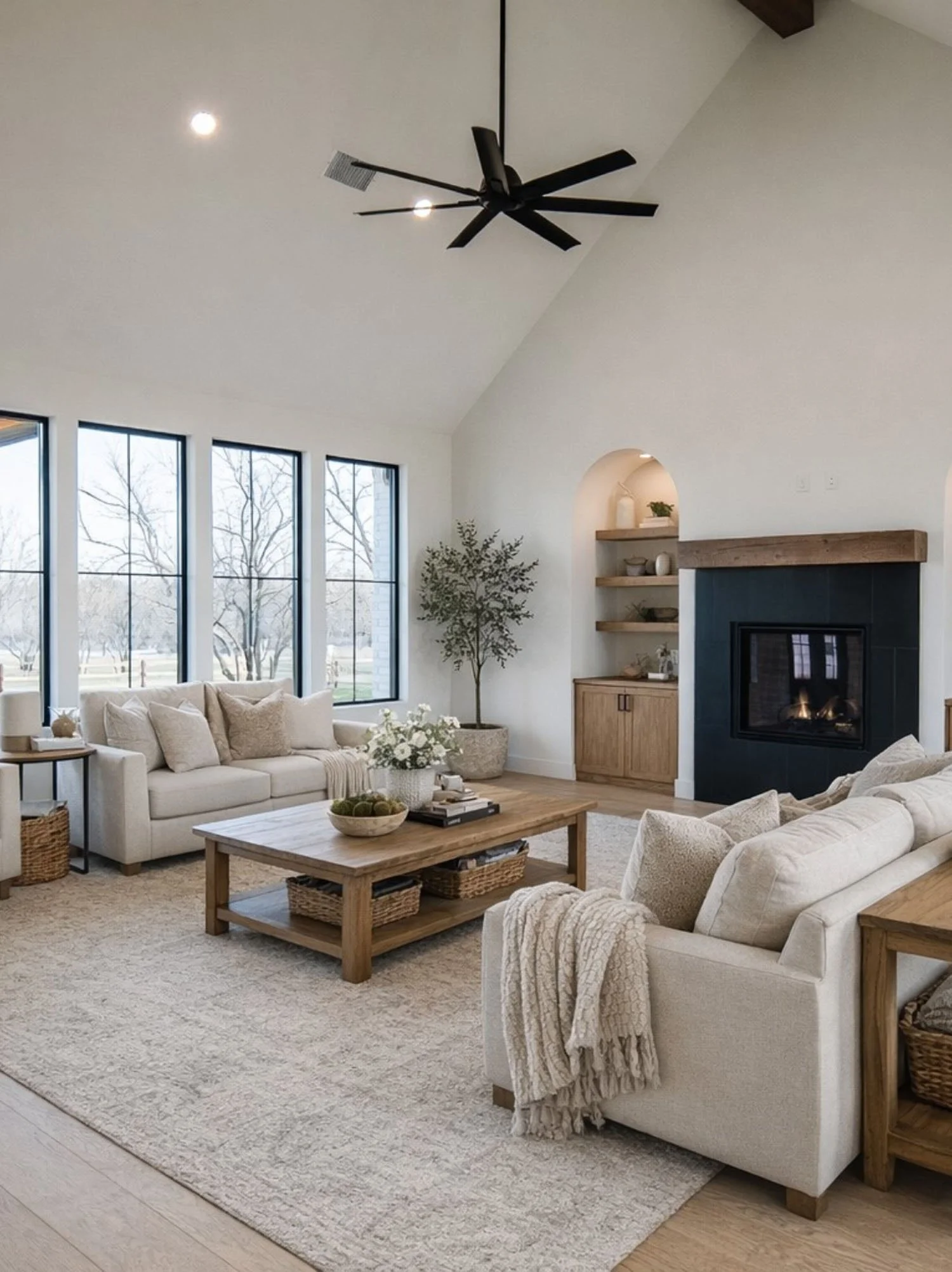 A bright, open-concept living room with a vaulted ceiling, a black fireplace, and light neutral furniture.