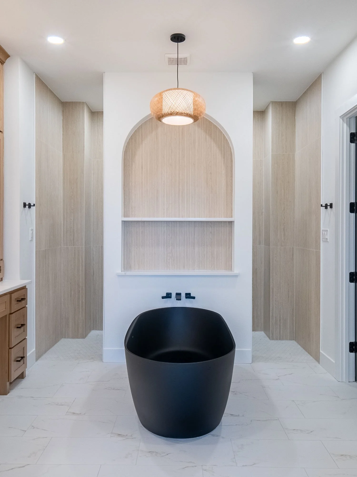 A modern bathroom featuring a freestanding black bathtub, an arched wall niche with shelving, and a woven pendant light fixture.