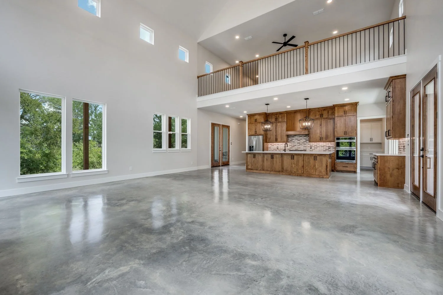 Open-concept home interior featuring polished concrete floors, stained wood cabinetry, and a lofted area overlooking the kitchen and living space.