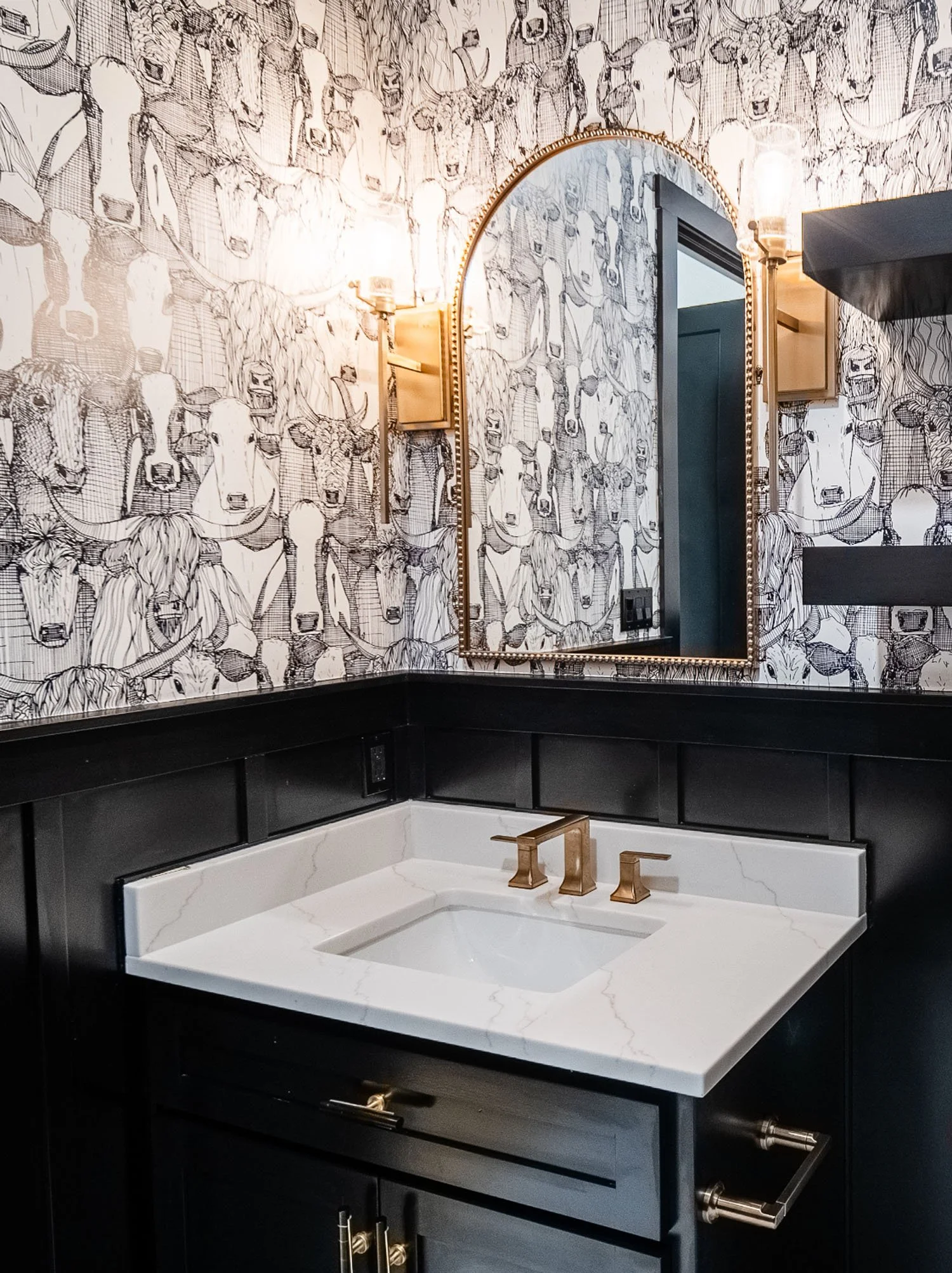 A bathroom featuring black and white cow-patterned wallpaper, a black vanity with a white quartz countertop, and gold hardware.