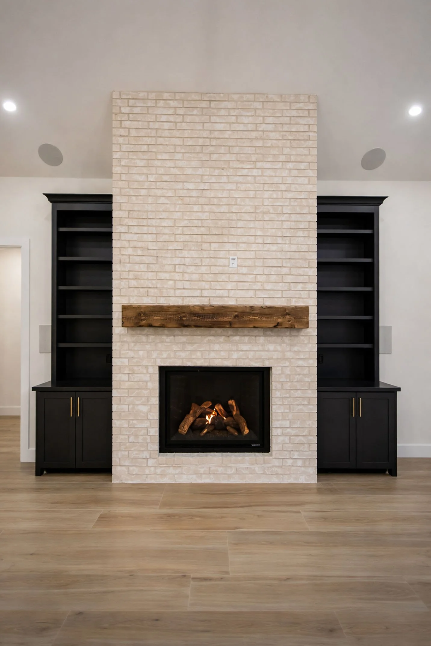 A living room focal point featuring a floor-to-ceiling light brick fireplace with a rustic wood mantel, flanked by built-in matte black cabinetry and shelving.