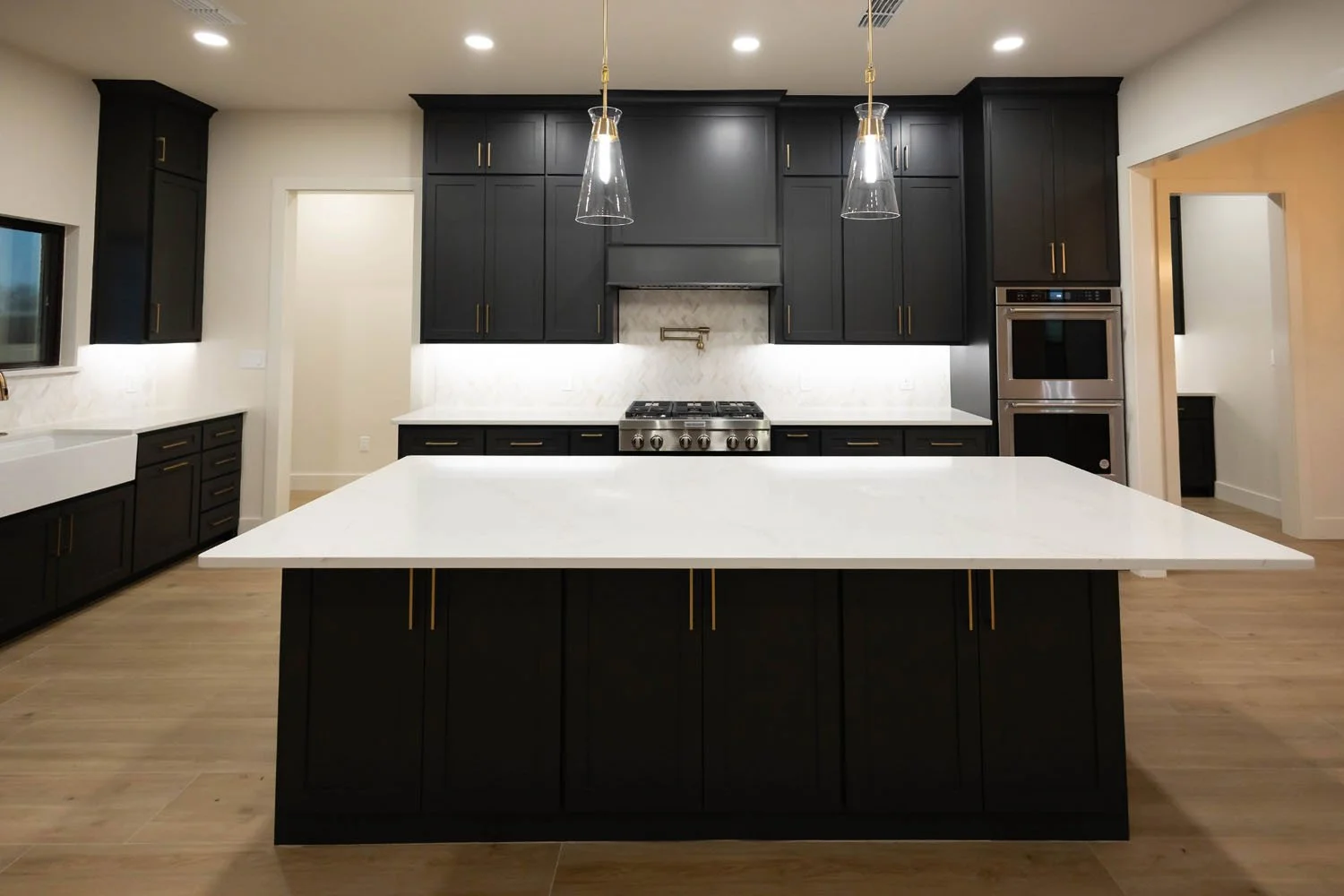 A kitchen with matte black cabinets, white quartz countertops, a large center island, and high-contrast gold hardware.